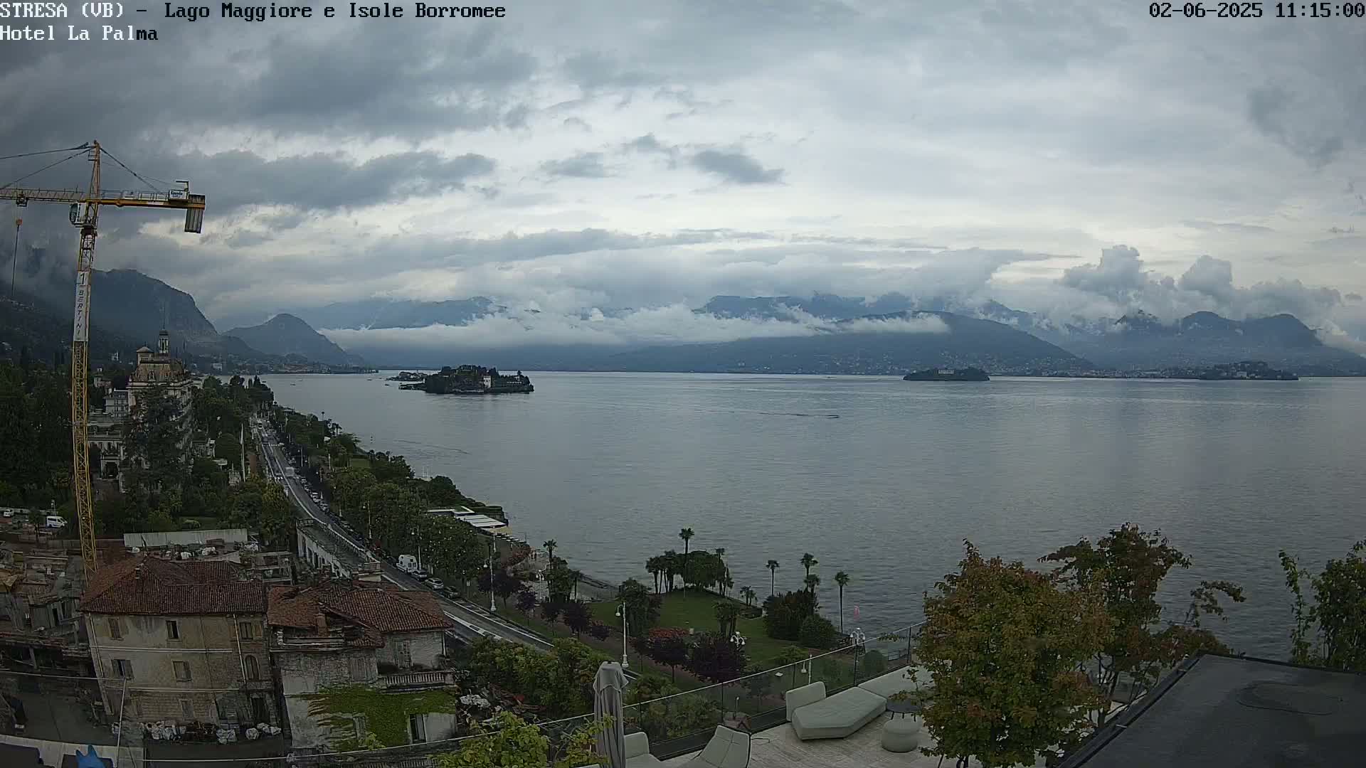 A large body of water with islands and mountains in the background under a cloudy sky, viewed from a high vantage point overlooking a town with a construction crane.