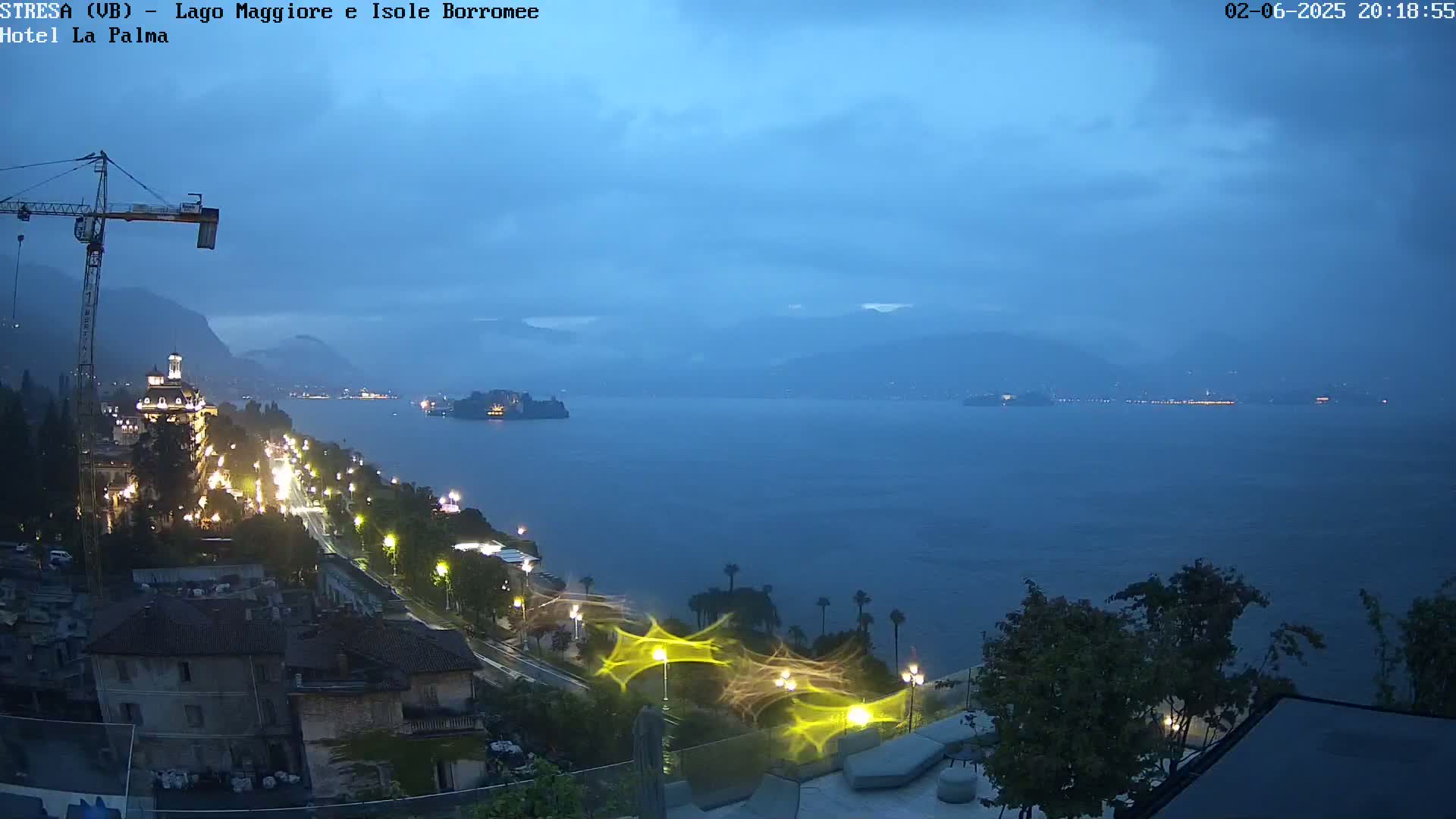 A nighttime view of a lakeside town with a large body of water, mountains in the distance, and overcast skies.