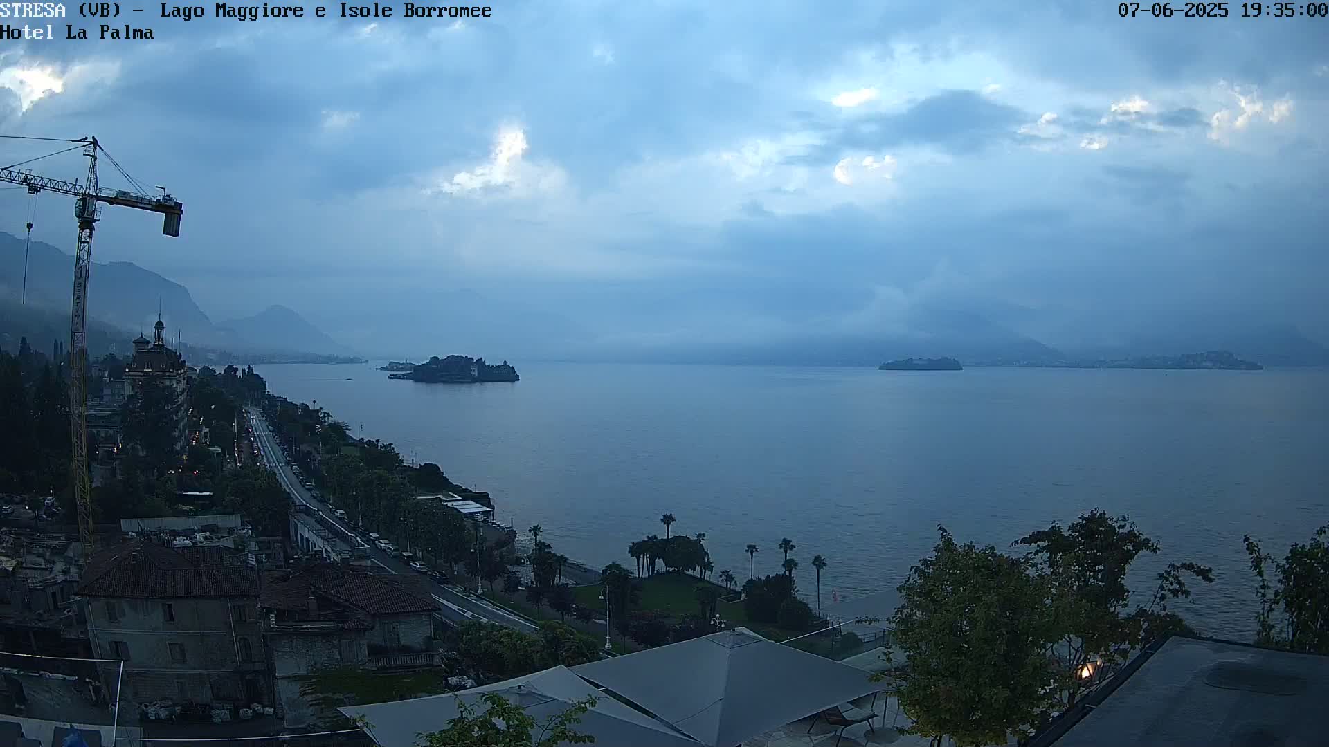 A twilight view of a large body of water with islands in the distance, a shoreline with buildings and trees, and a construction crane visible on the left.