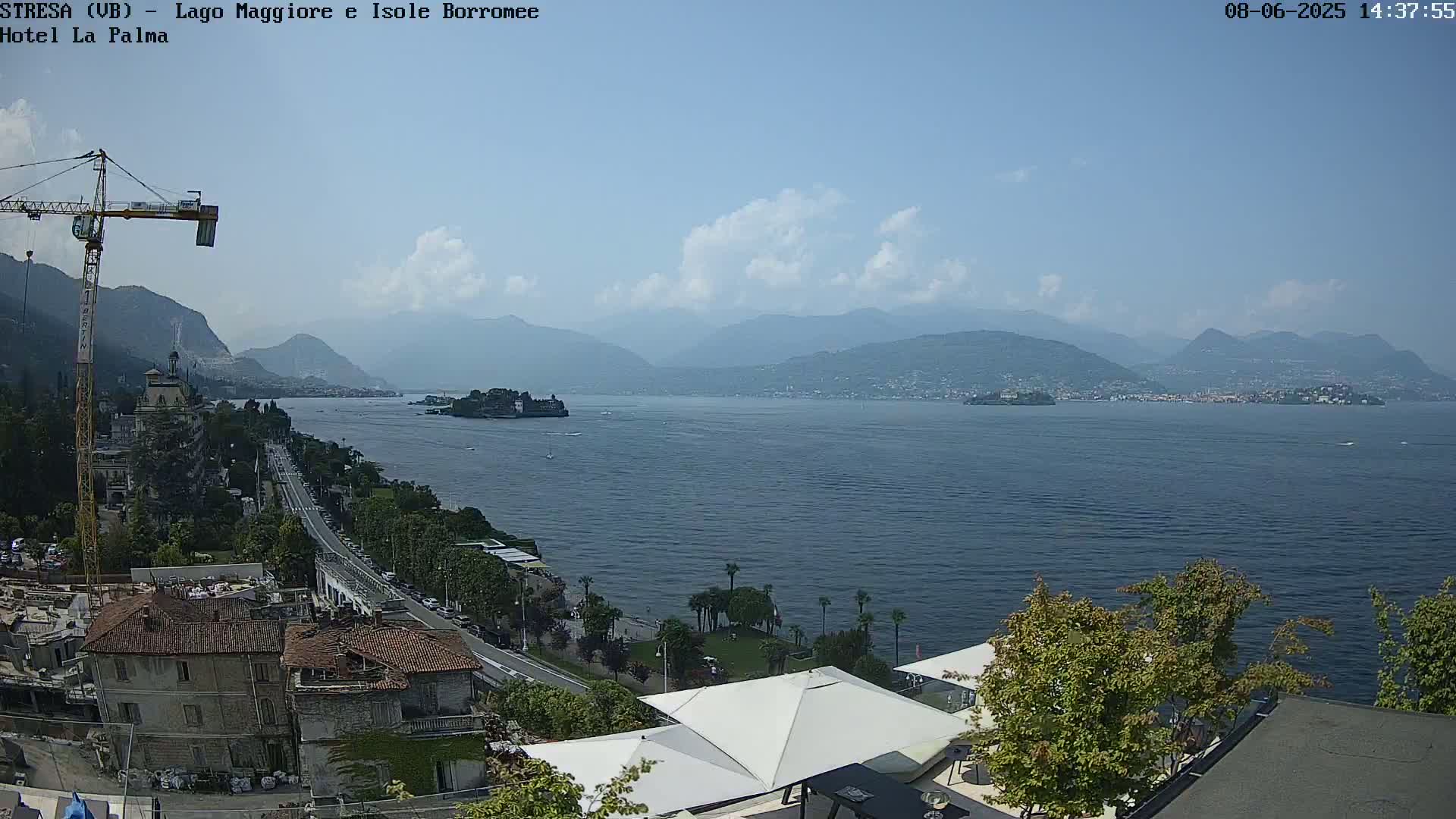A sunny day overlooking a large lake with mountains in the background, a town on the lakeshore, and a construction crane visible in the foreground.