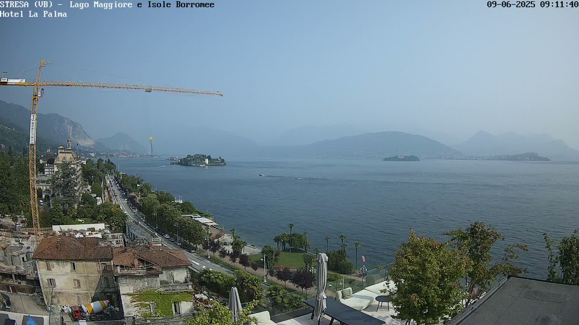 A hazy, sunny day overlooking a calm lake, with a town, a construction crane, and distant mountains visible.