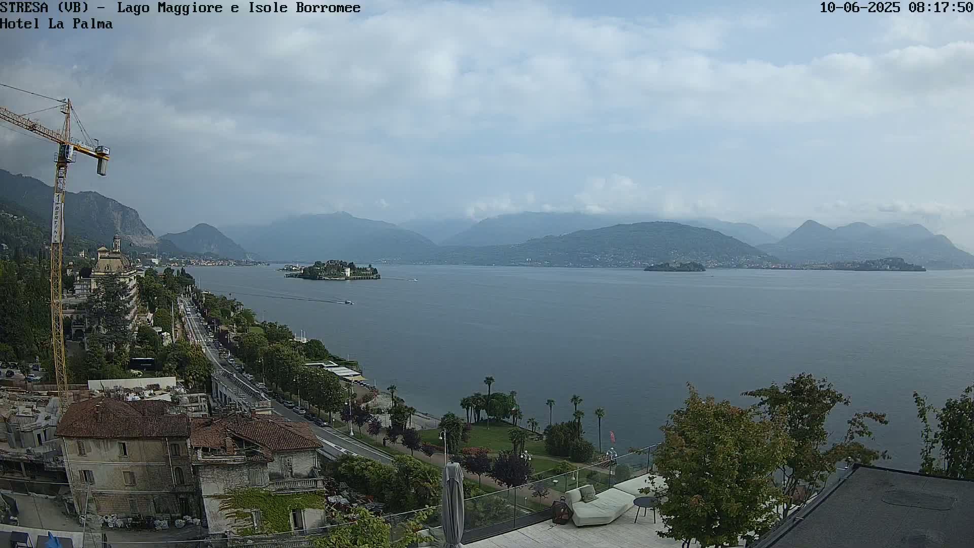 A partly cloudy day overlooks a large lake with mountains in the background, a town on the shore, and an island visible in the middle distance.