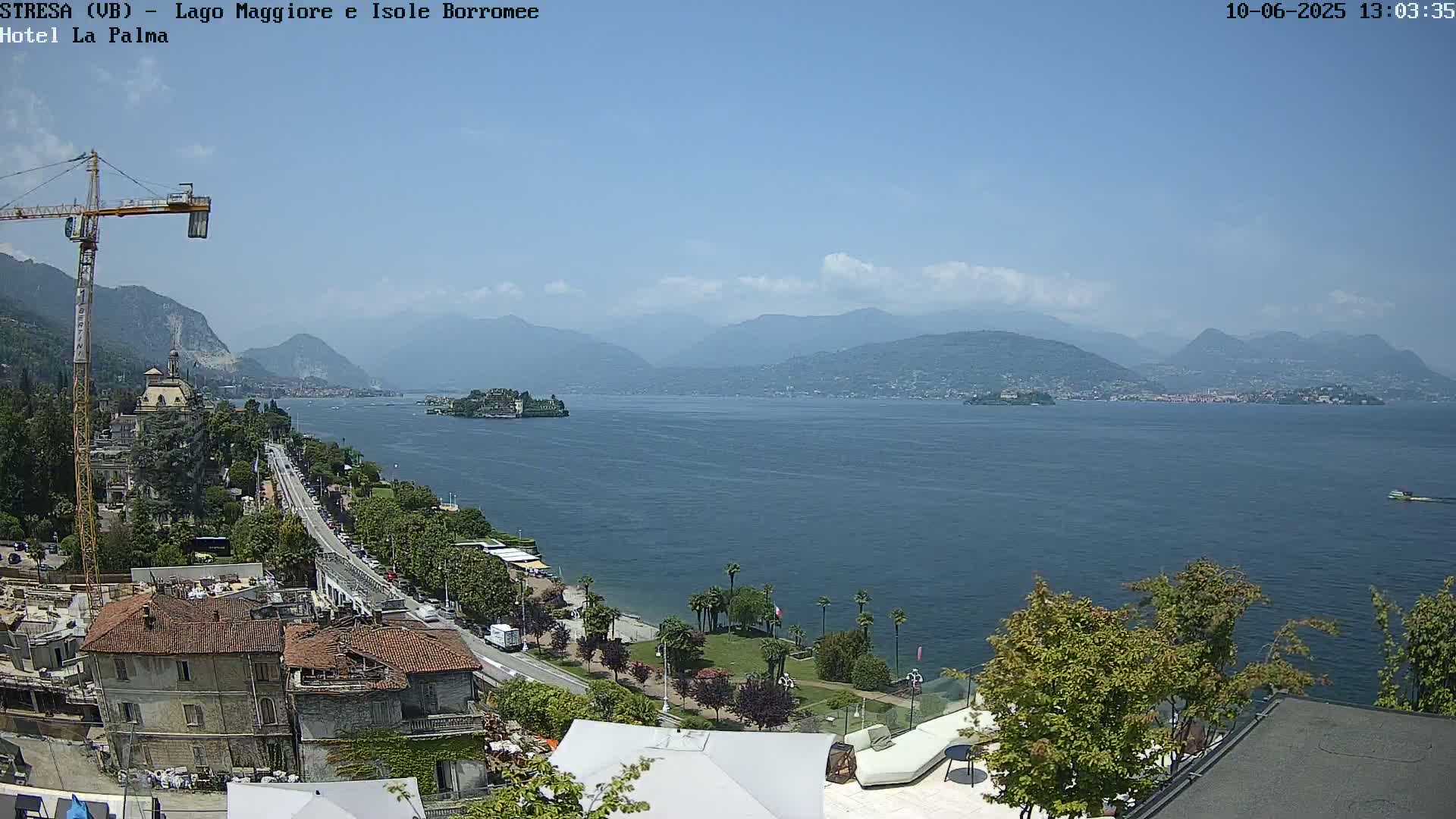 A sunny view of a lake with mountains in the background, a town on the shoreline, and a construction crane visible.