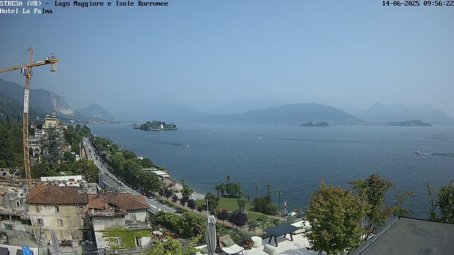 A sunny day overlooking a large lake with islands and mountains in the distance, showing a town with buildings and a road along the shoreline.