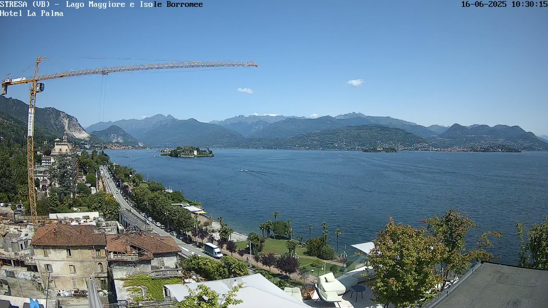 A large body of water stretches toward distant mountains under a clear blue sky, with a crane visible in the foreground and a town nestled along the shoreline.