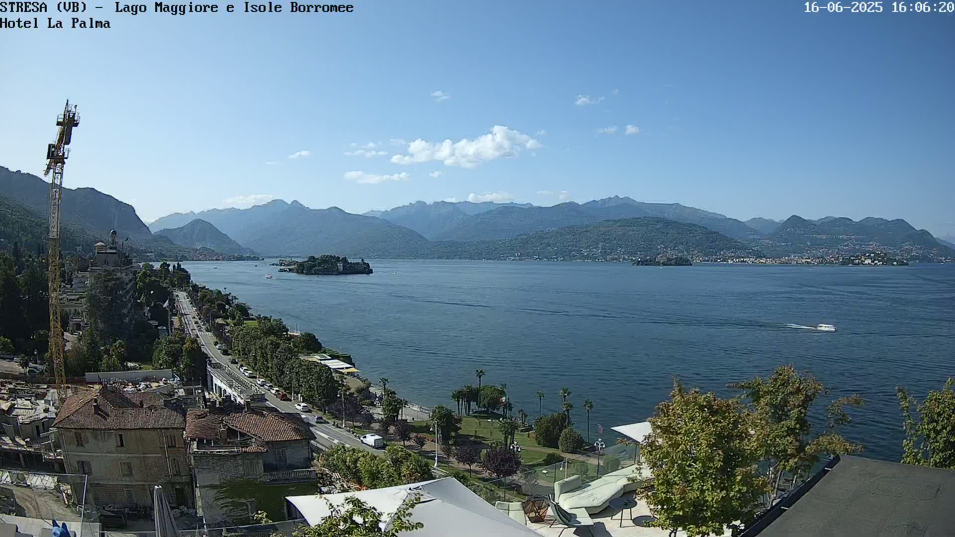 A sunny day overlooking a large lake with mountains in the distance, a small boat on the water, and a town visible along the lakeshore.