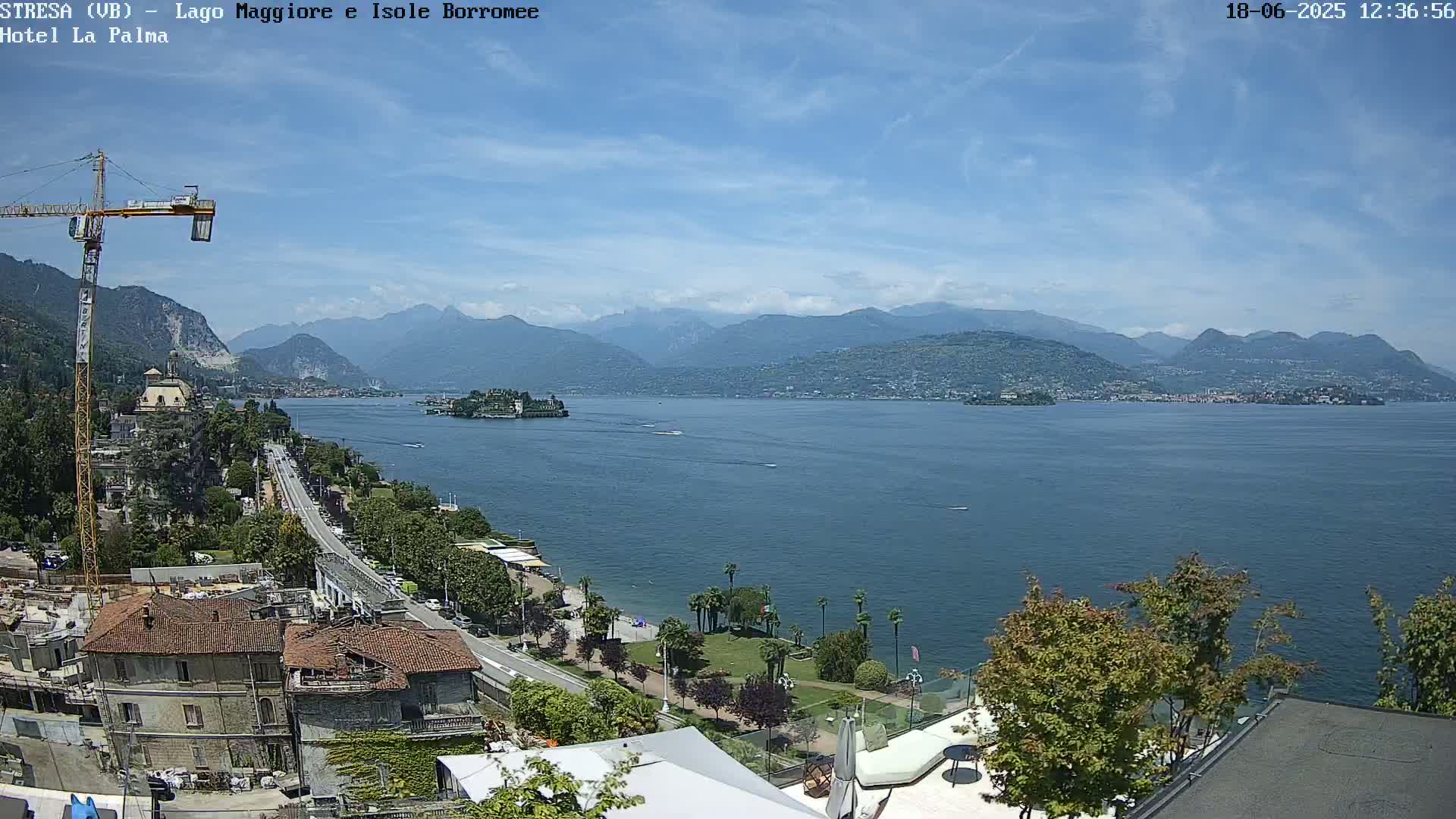 A sunny day overlooking a large lake with mountains in the distance, a shoreline with buildings and trees, and a construction crane visible.