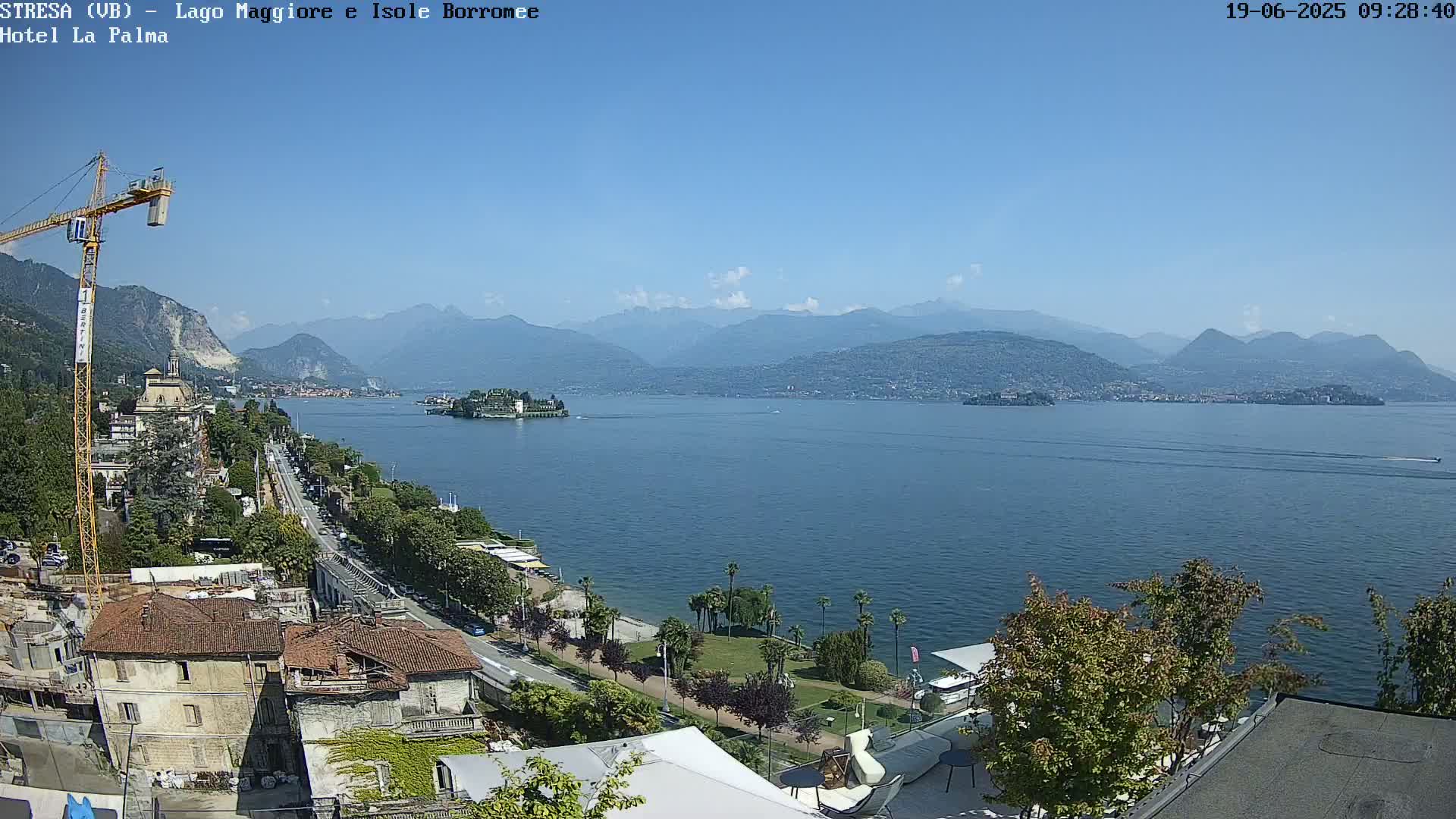 A sunny view of a lake with islands and mountains in the distance, overlooking a waterfront road and buildings.