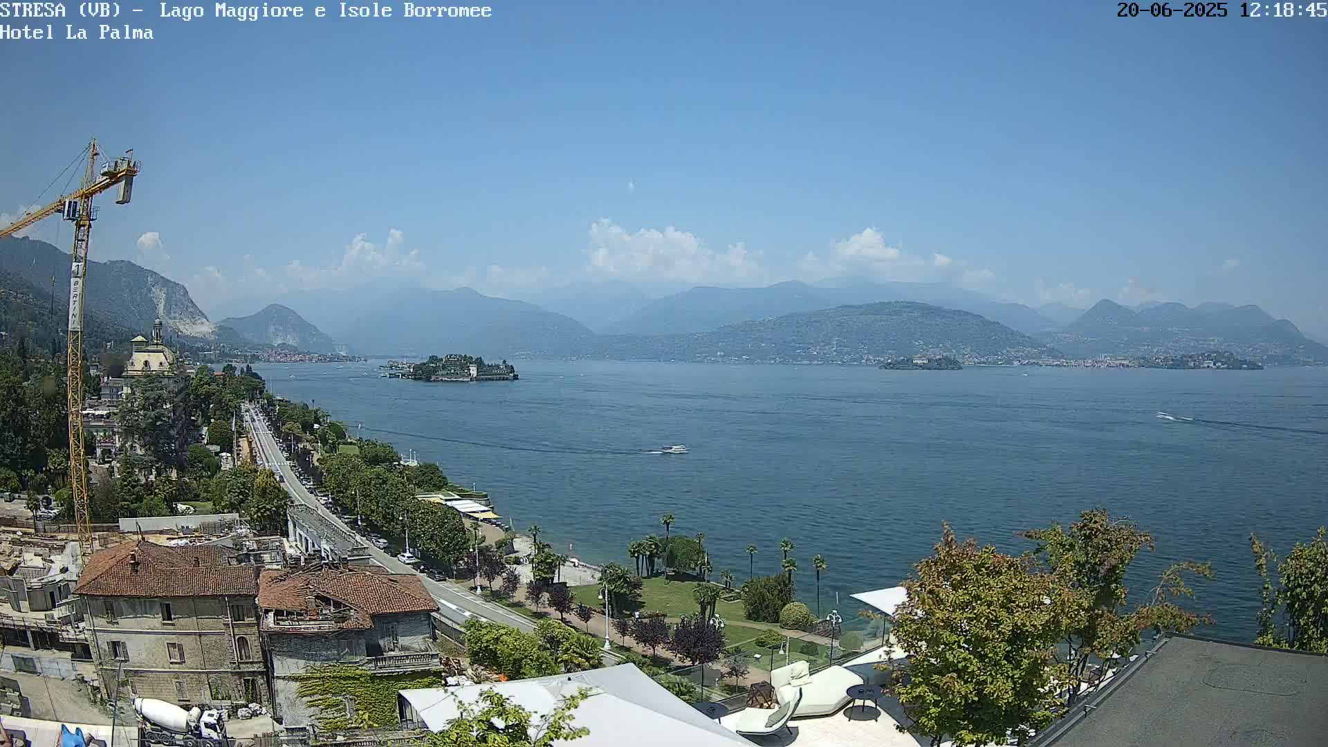 A sunny day overlooking a large lake with mountains in the background, a town along the shoreline, and a construction crane visible near the foreground.
