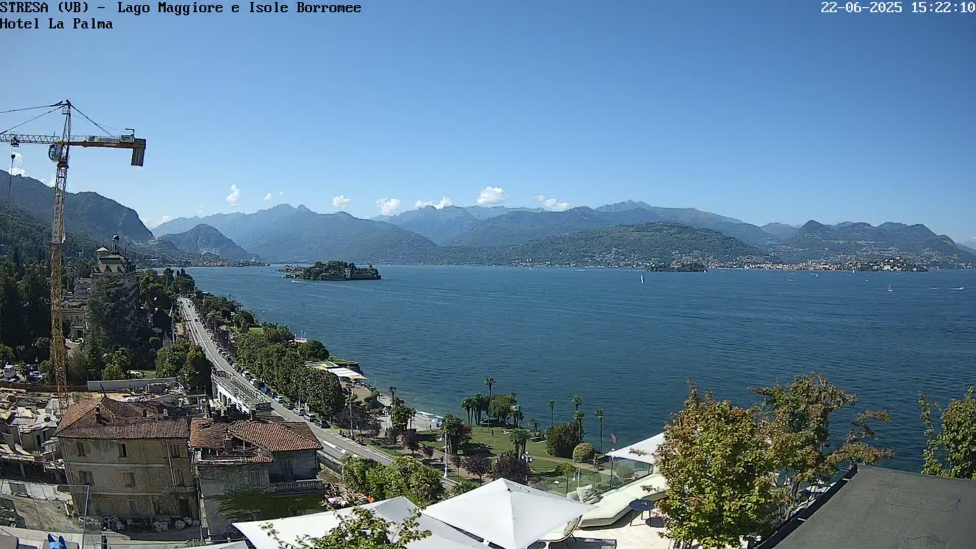 A sunny day overlooking a large lake with mountains in the background, a town visible along the shore, and a construction crane near the foreground.