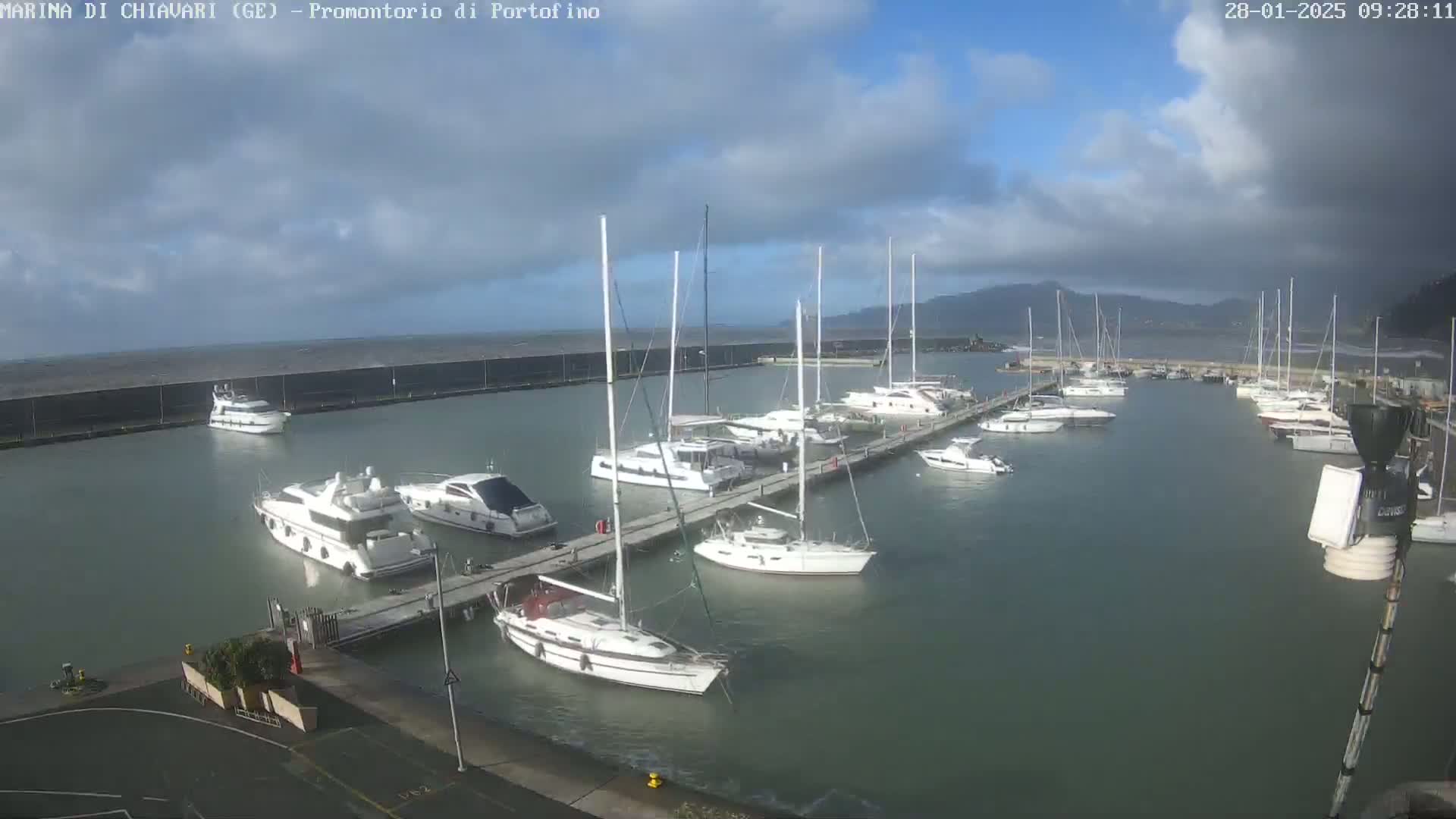 A marina filled with numerous sailboats and motorboats under a partly cloudy sky.