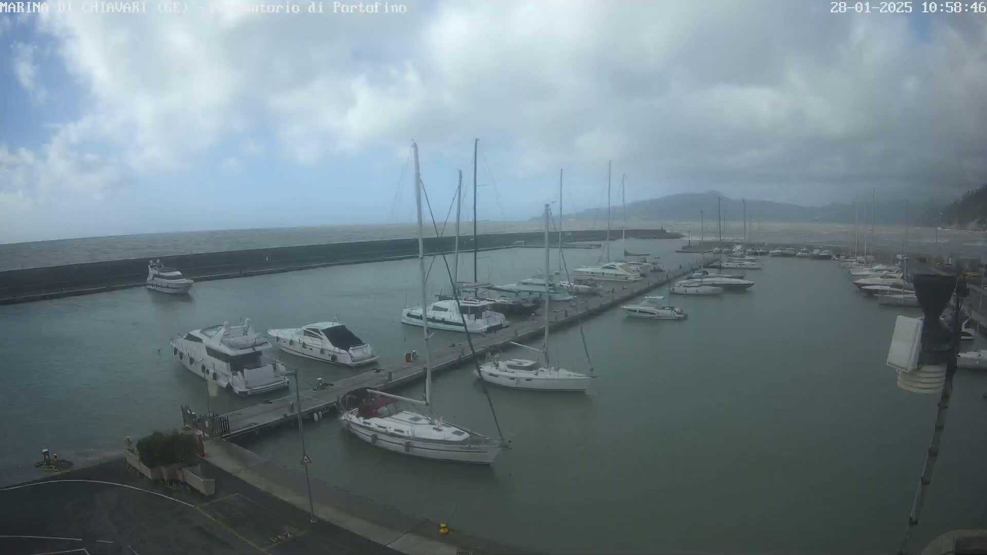 A marina filled with yachts and sailboats under a cloudy sky with choppy water visible beyond a breakwater.
