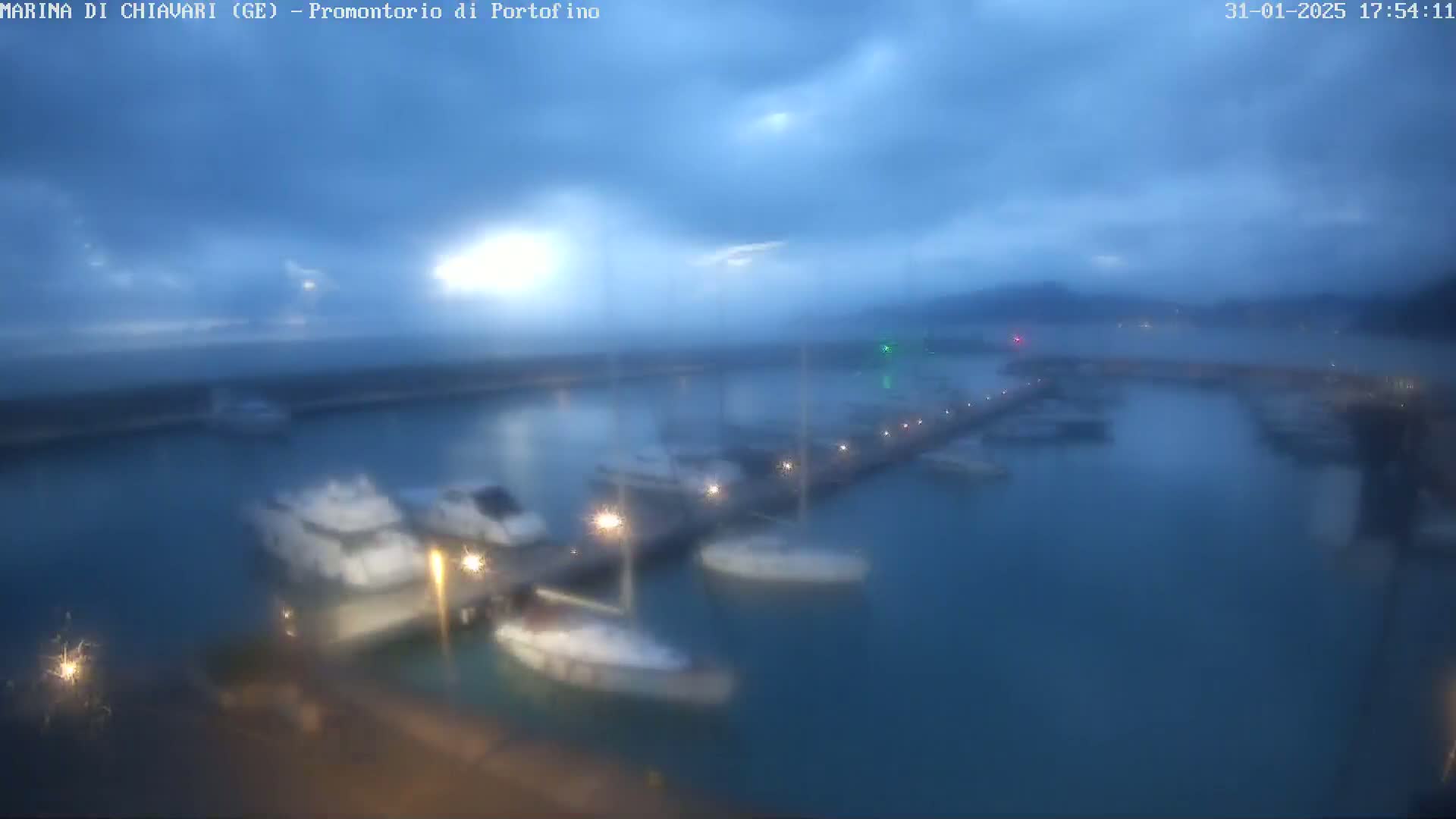 A marina filled with boats is seen under a hazy, overcast sky at dusk.