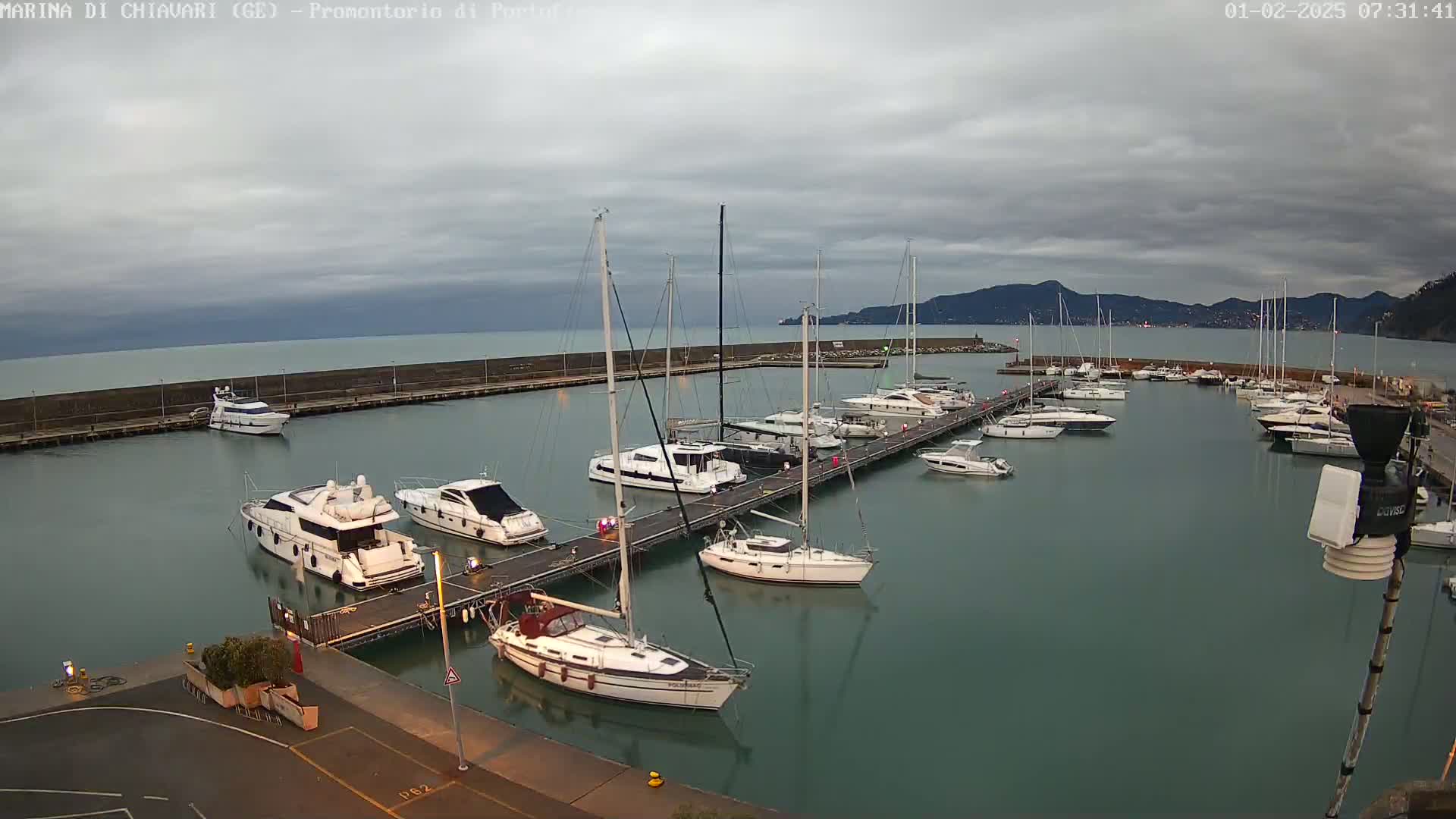 A marina filled with numerous yachts and sailboats is shown under a cloudy sky.