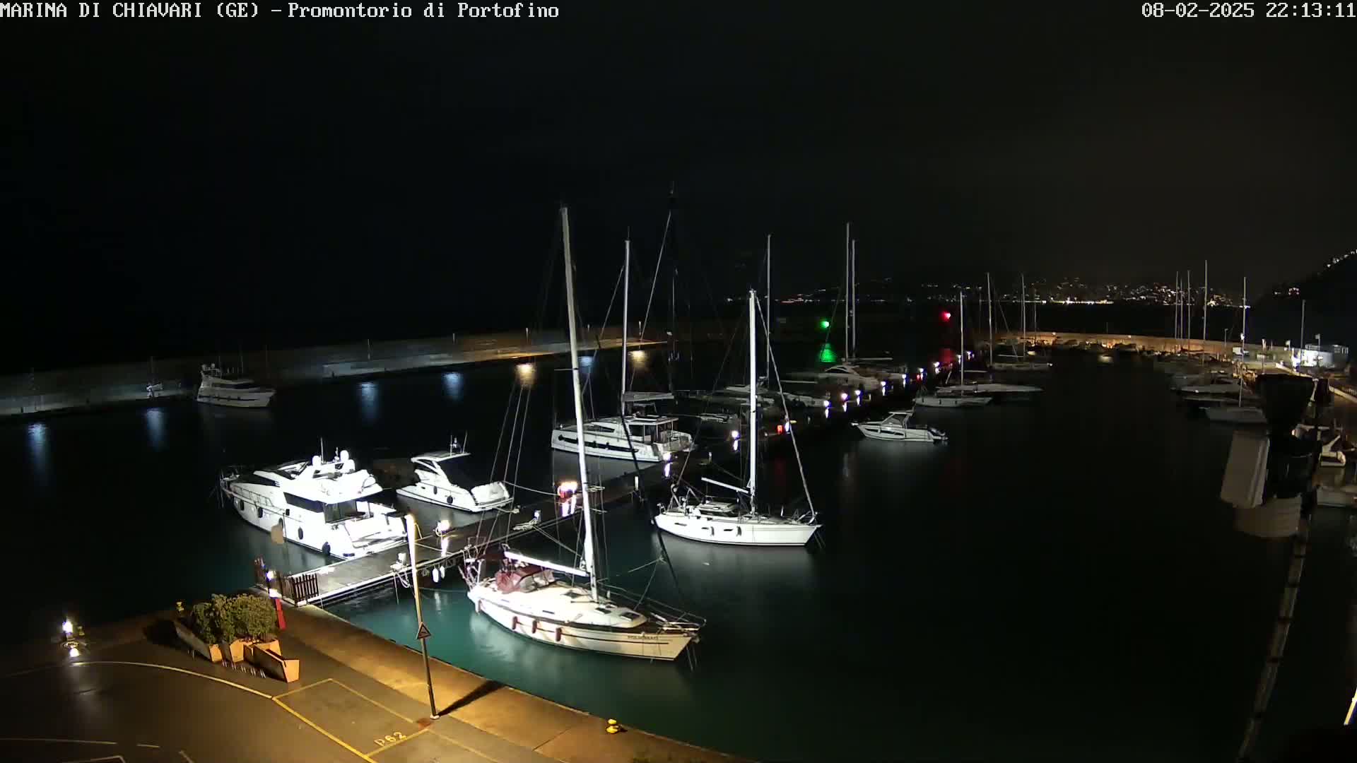 Many sailboats and yachts are docked at a marina at night, under partly cloudy skies.