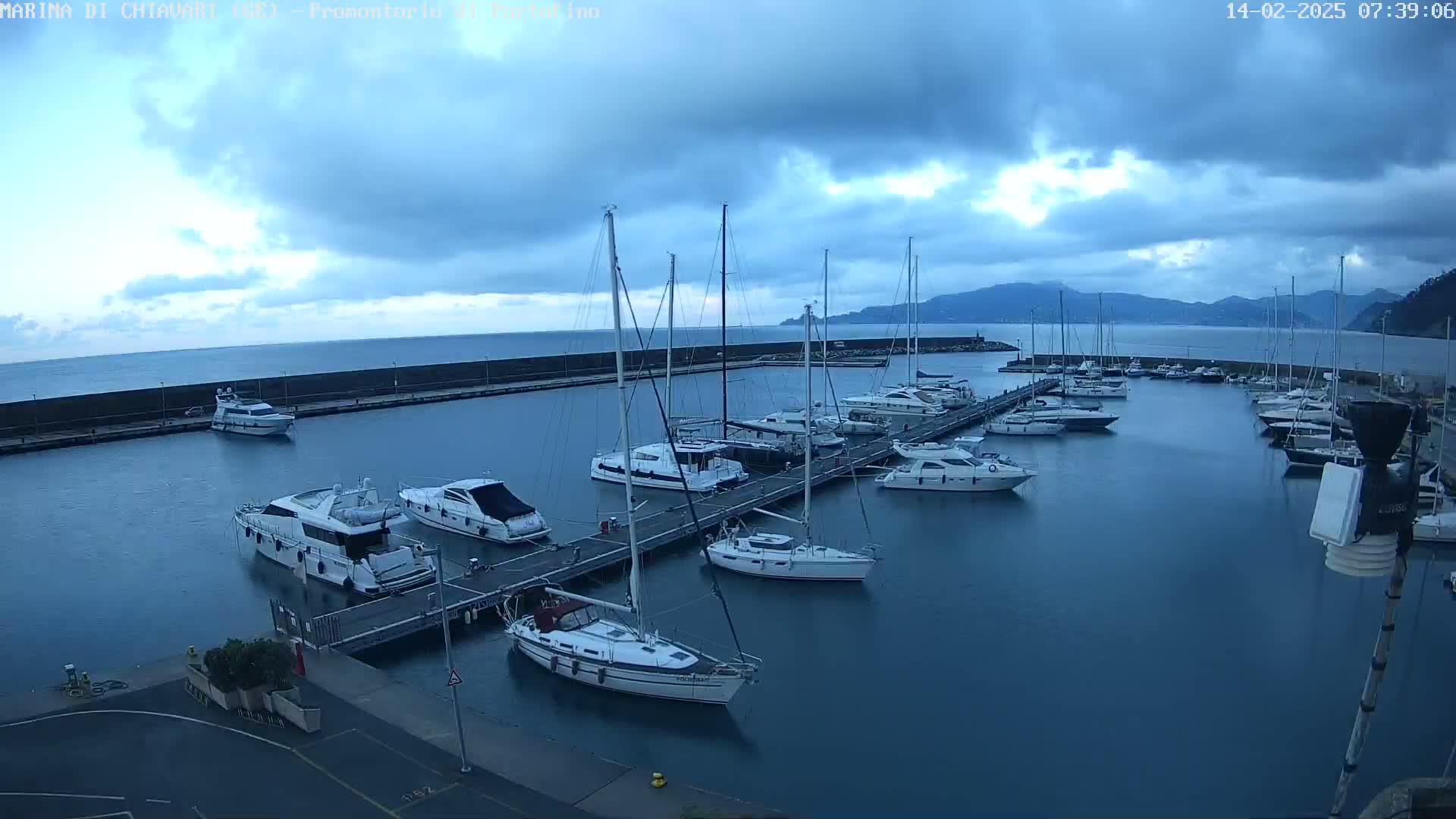 A marina filled with numerous sailboats and motorboats under a cloudy sky.