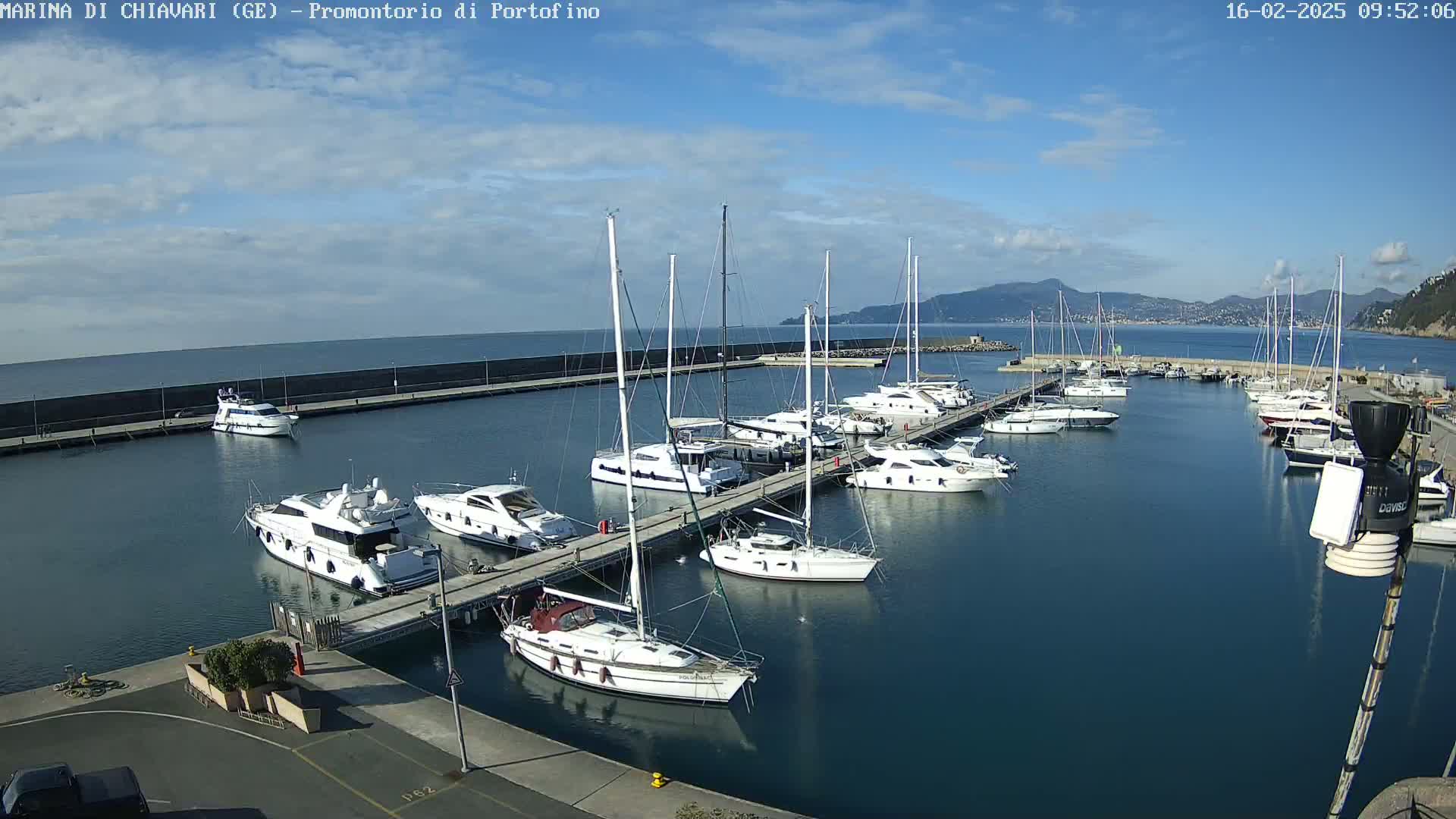 A marina filled with numerous yachts and sailboats on a partly cloudy day, with mountains visible in the distance.