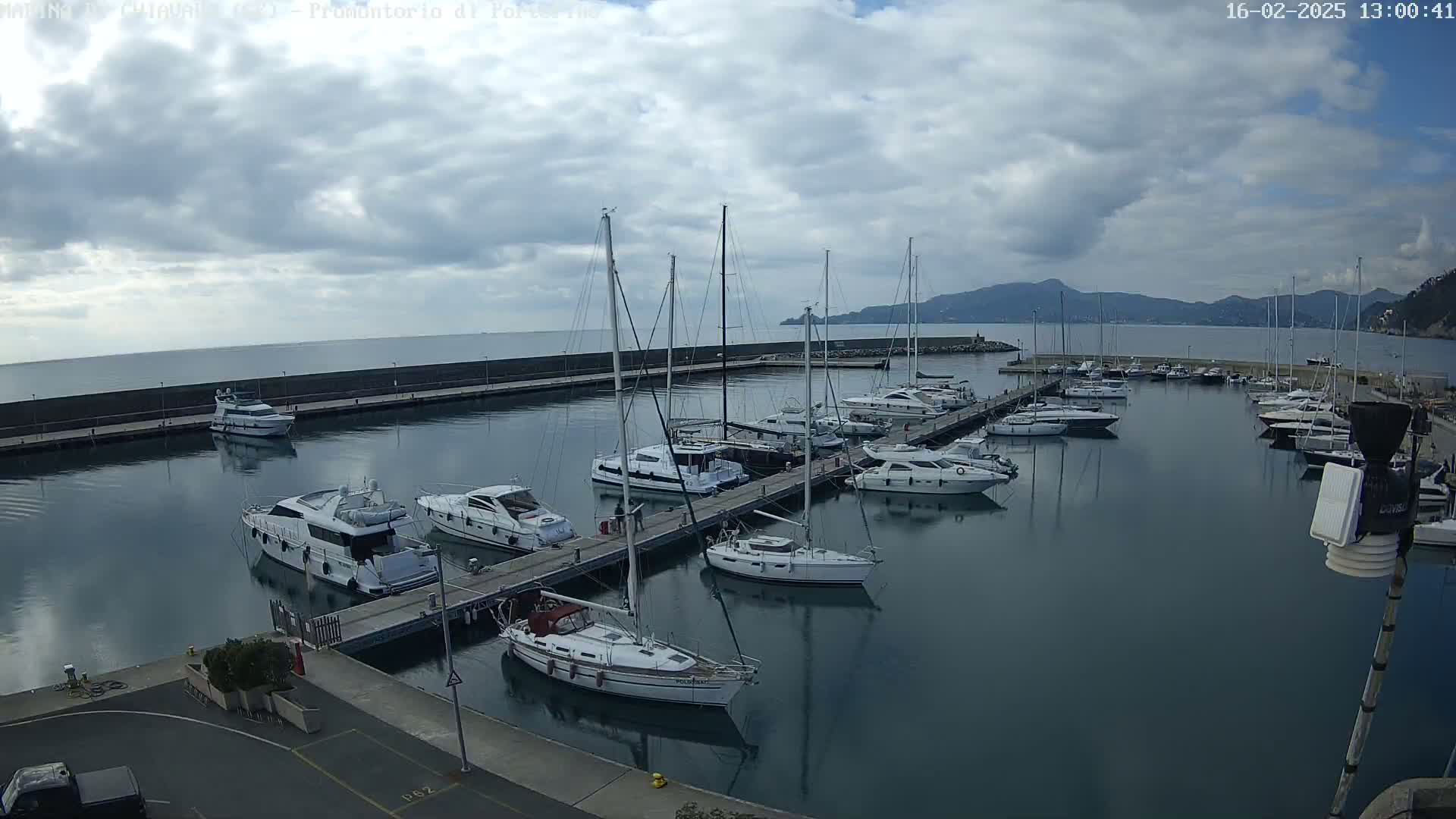 A marina filled with numerous sailboats and motorboats is seen under a cloudy sky.