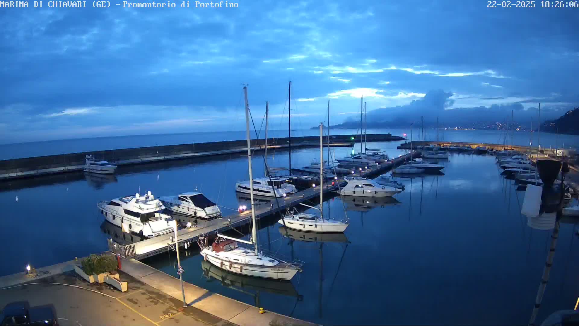 A marina filled with sailboats and motorboats at twilight under a mostly clear blue sky.