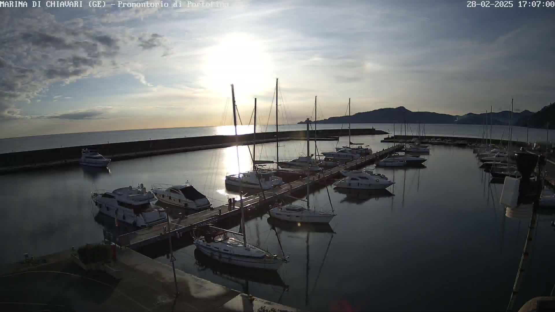 A marina filled with sailboats and motorboats at sunset under a partly cloudy sky.