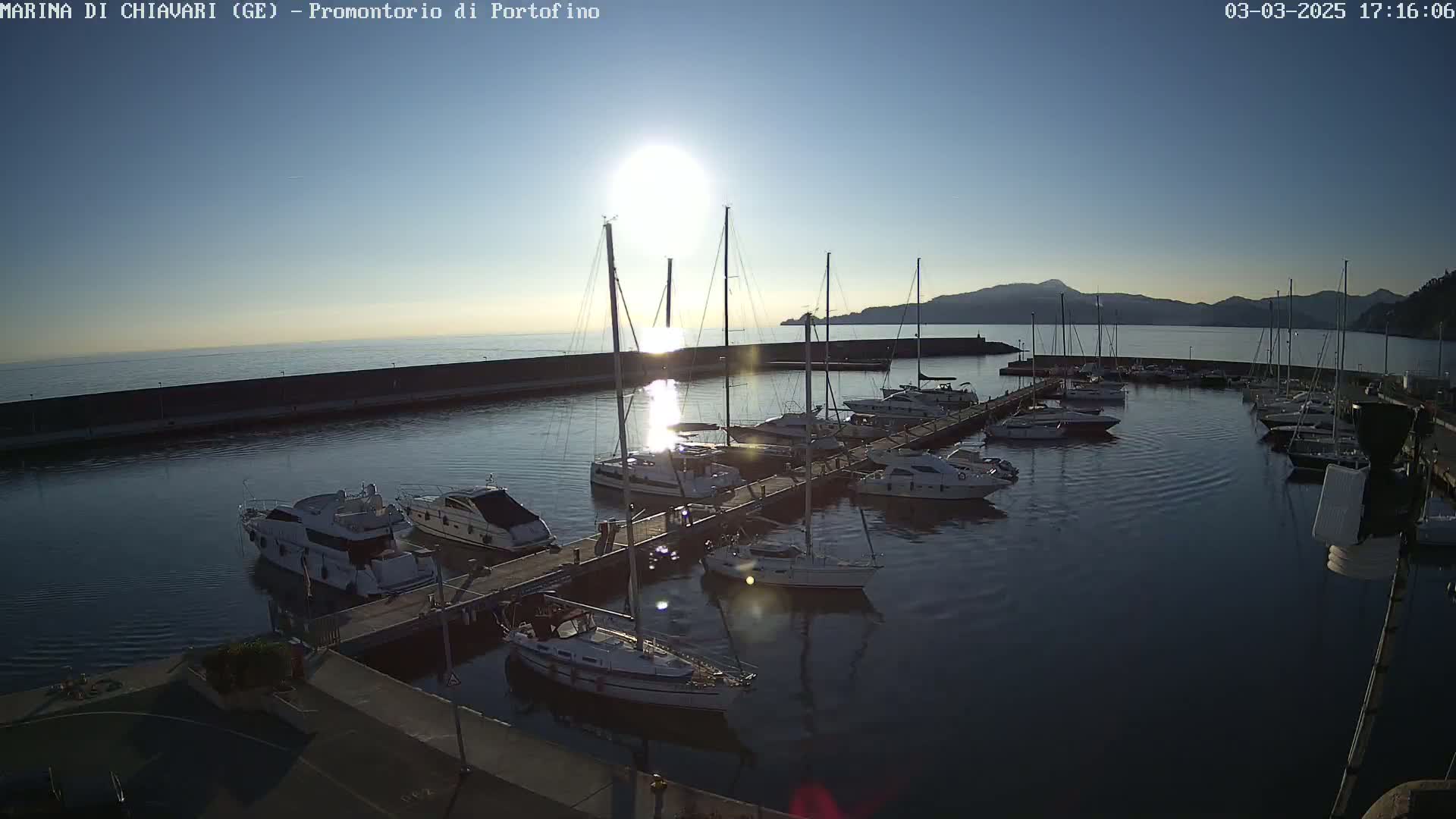A marina filled with sailboats and motorboats is seen at sunset under a clear sky.
