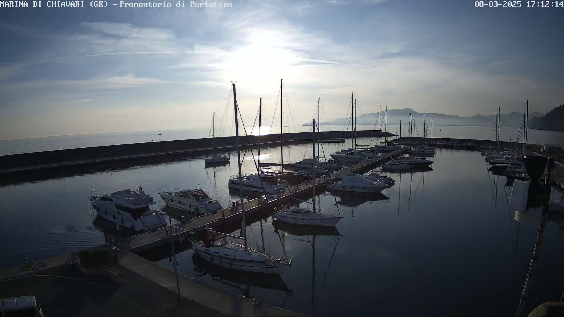 A marina filled with sailboats and motorboats is seen at sunset under a mostly clear sky.