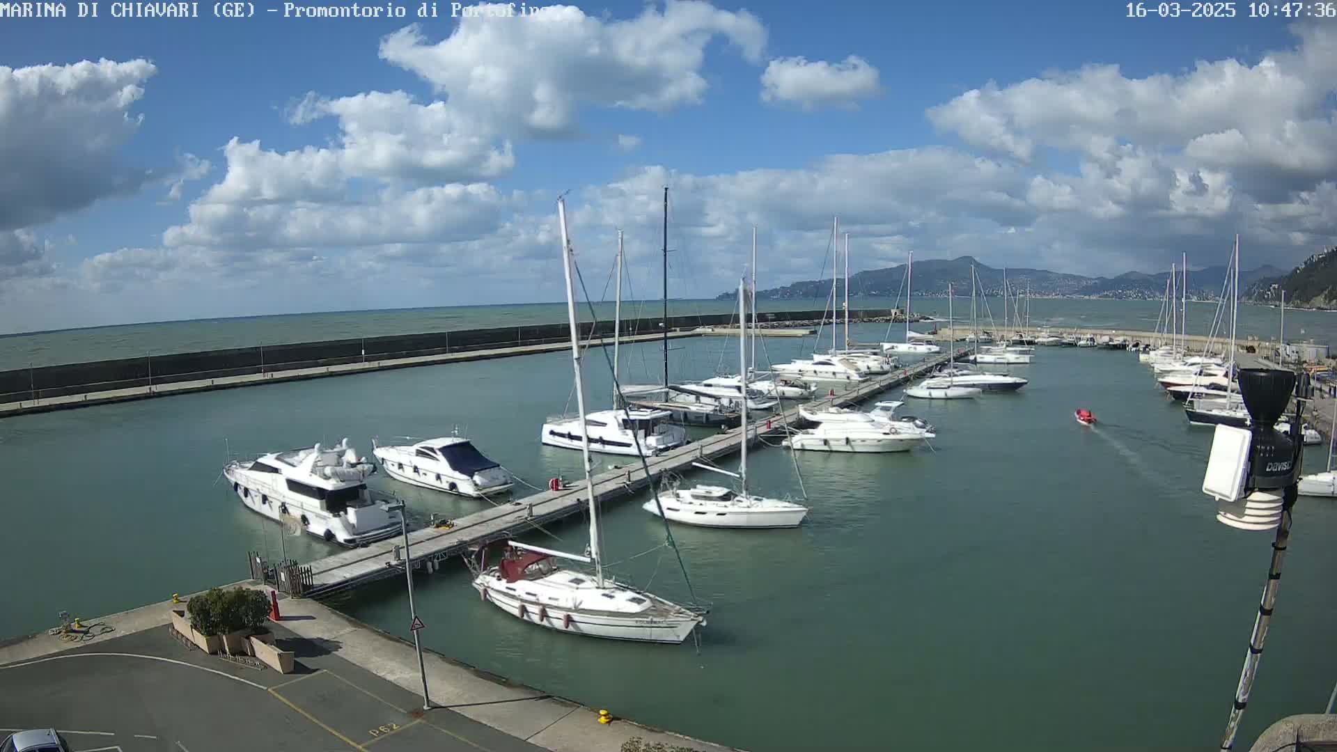 A marina filled with numerous sailboats and motorboats is seen under a partly cloudy sky.