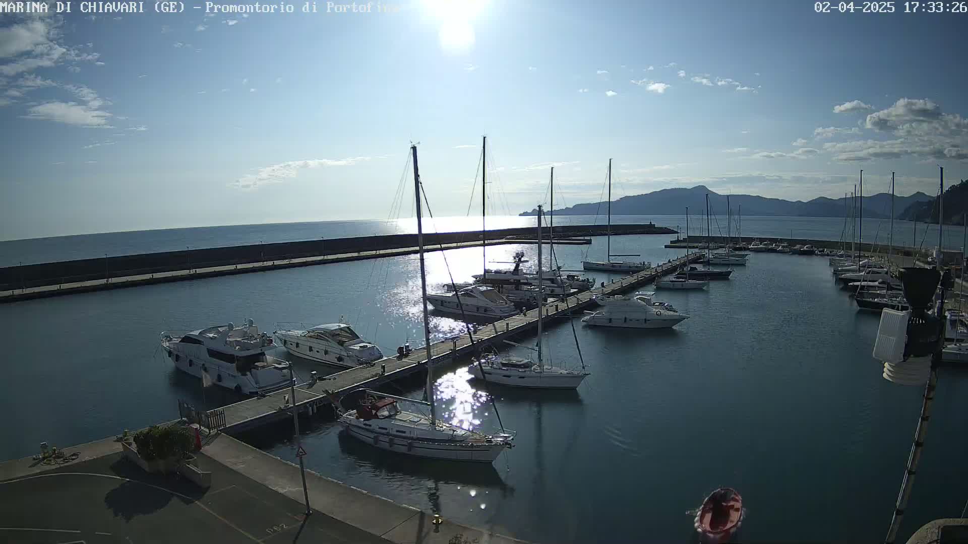 A marina filled with sailboats and motorboats is seen on a sunny day with a few clouds in the sky.