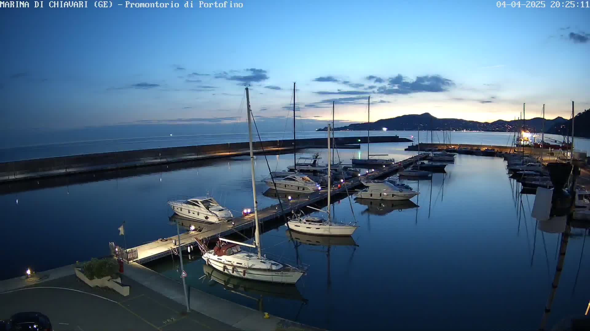 A marina at twilight, filled with sailboats and motor yachts docked along piers, under a mostly clear sky.