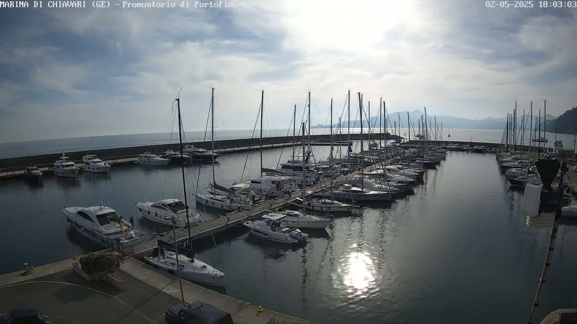 Many sailboats and motorboats are docked in a marina on a partly cloudy day.