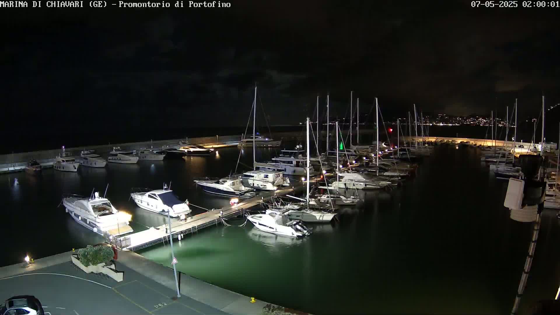 A marina filled with yachts and sailboats is shown at night under a dark, cloudy sky.