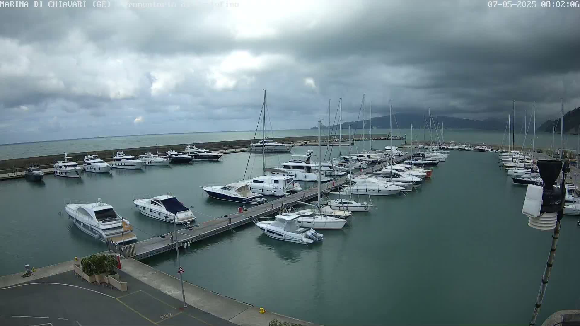 Many yachts and sailboats are docked in a marina under a cloudy sky.