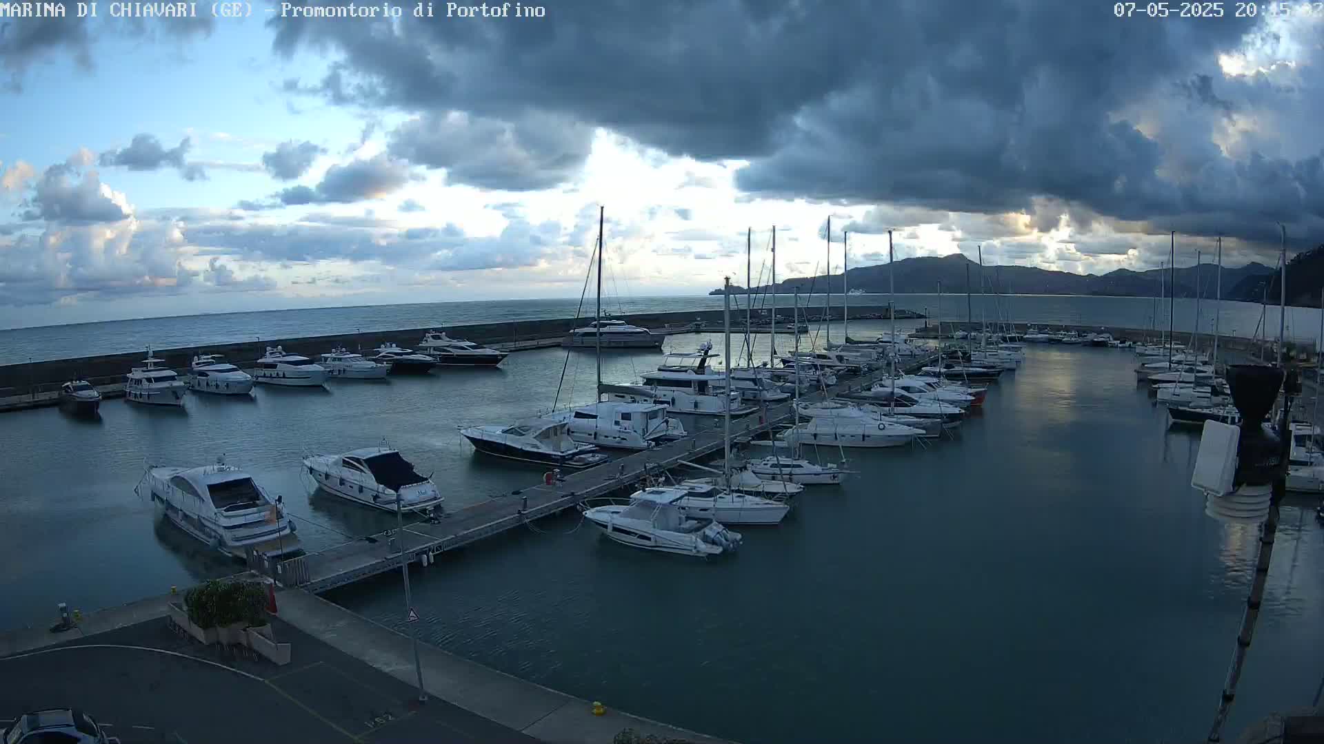 Many boats are docked in a marina under a partly cloudy sky.