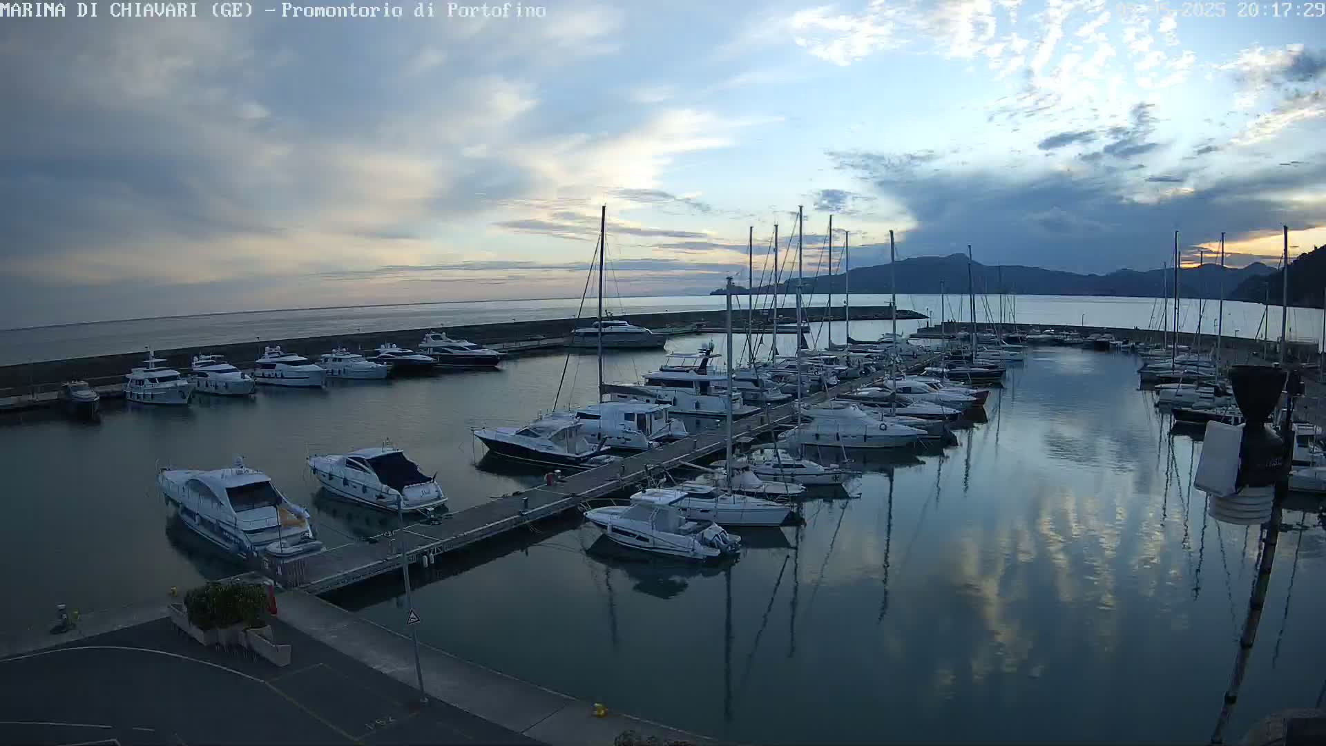 Many yachts and sailboats are docked in a marina at dusk under a partly cloudy sky.