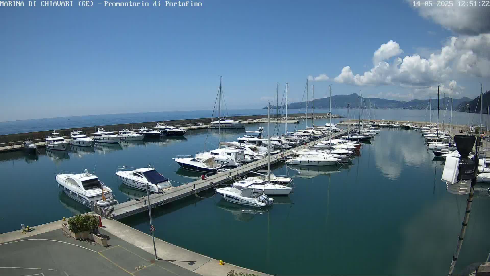 A marina filled with numerous yachts and sailboats on a sunny day with partly cloudy skies and calm water.