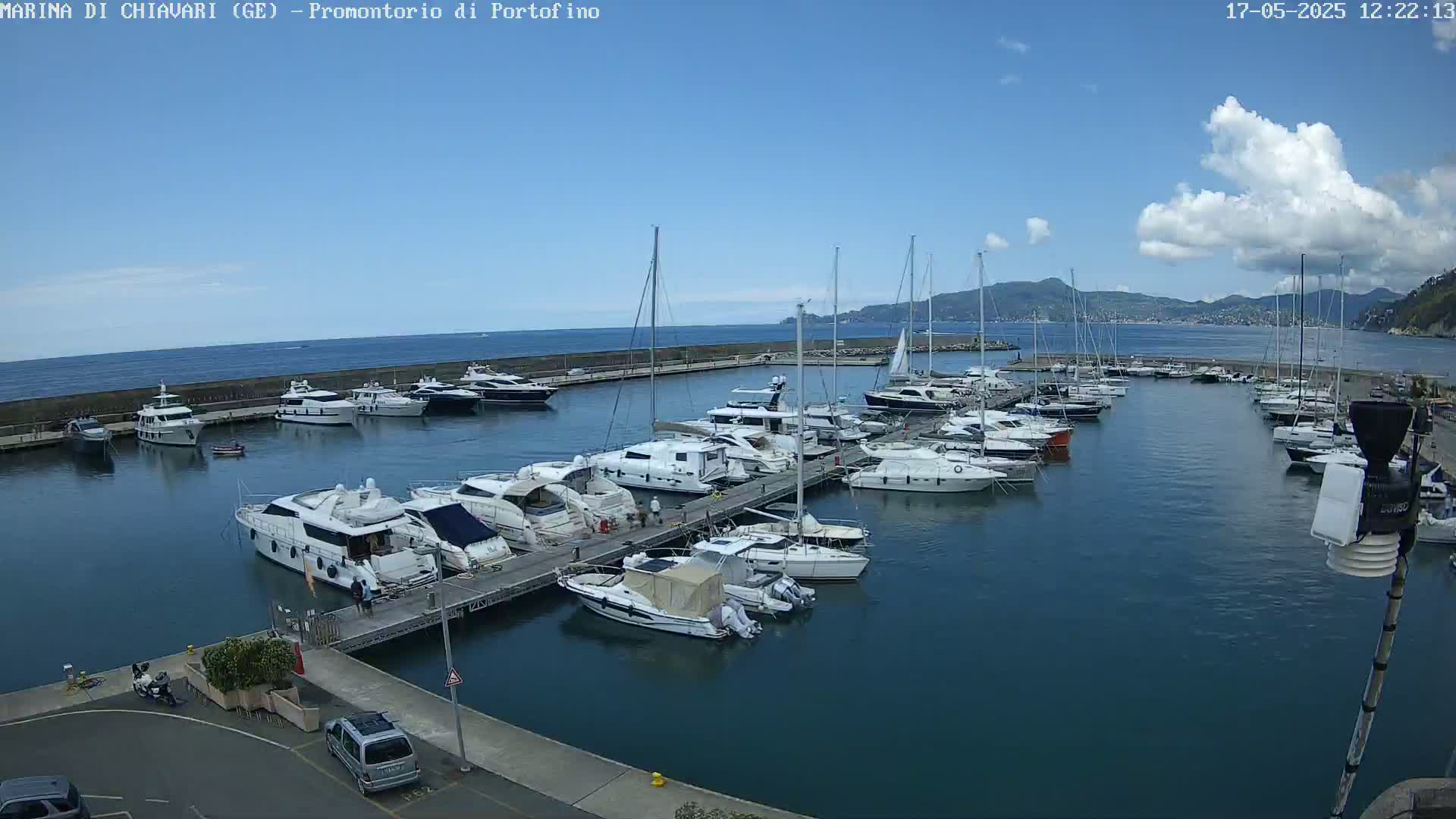 A marina filled with numerous yachts and sailboats is under a partly cloudy sky on a sunny day.