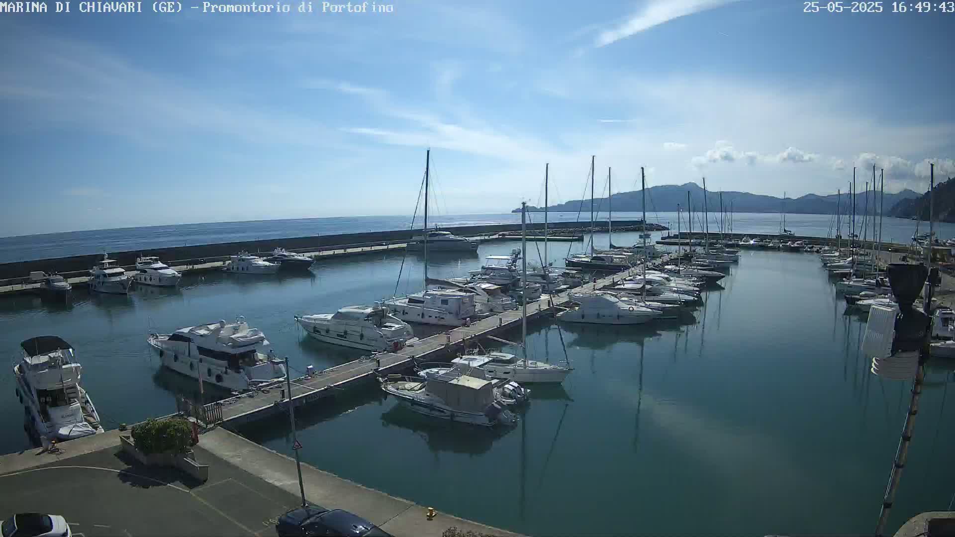 A marina filled with numerous yachts and sailboats is situated on calm, clear water under a mostly sunny sky.