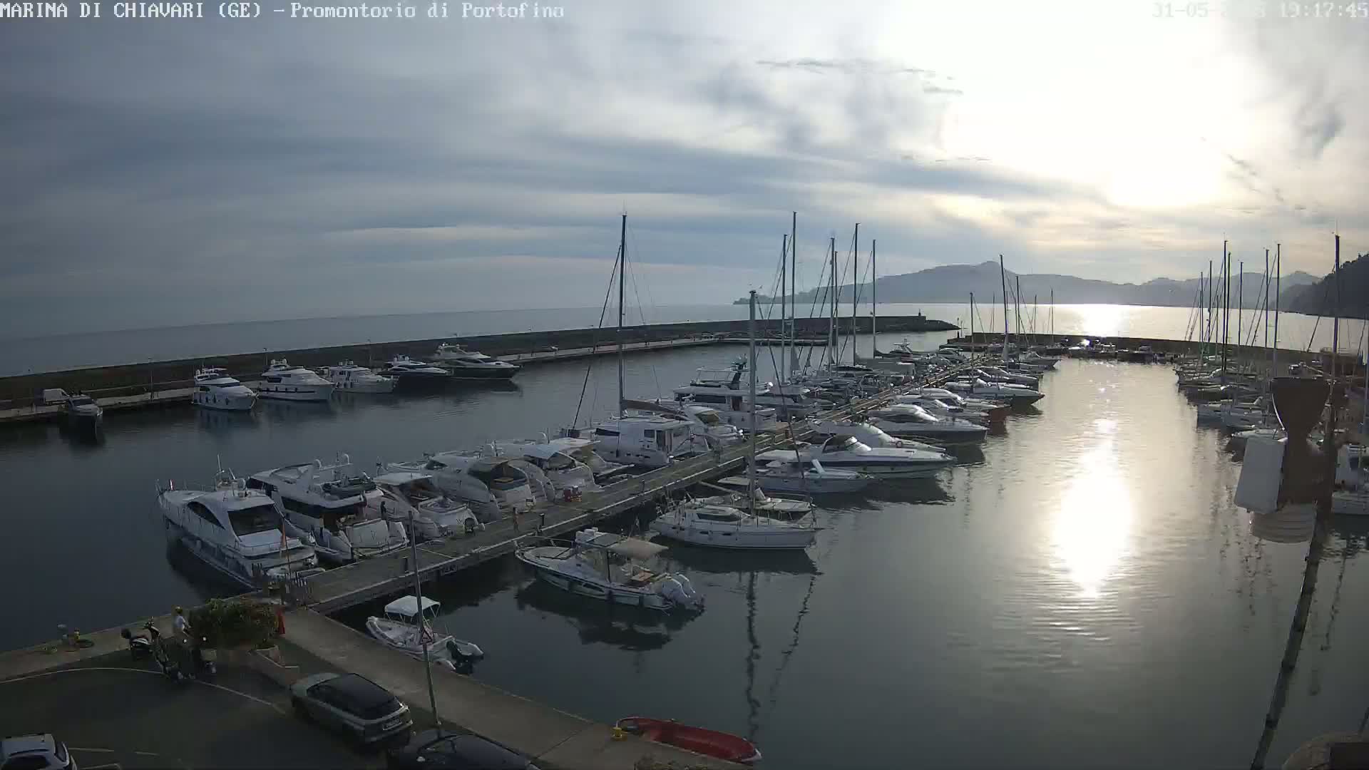A marina filled with numerous yachts and sailboats is situated on calm water under a partly cloudy sky.