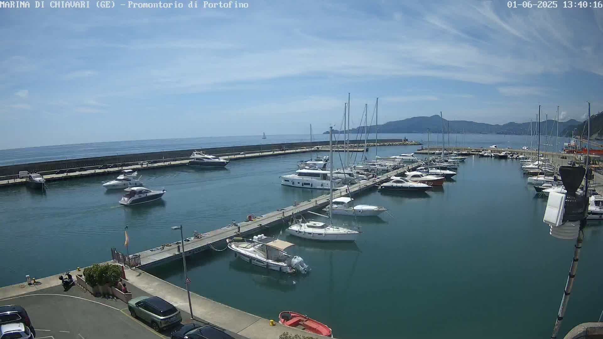 A marina filled with numerous yachts and sailboats is situated on calm, clear water under a mostly sunny sky.