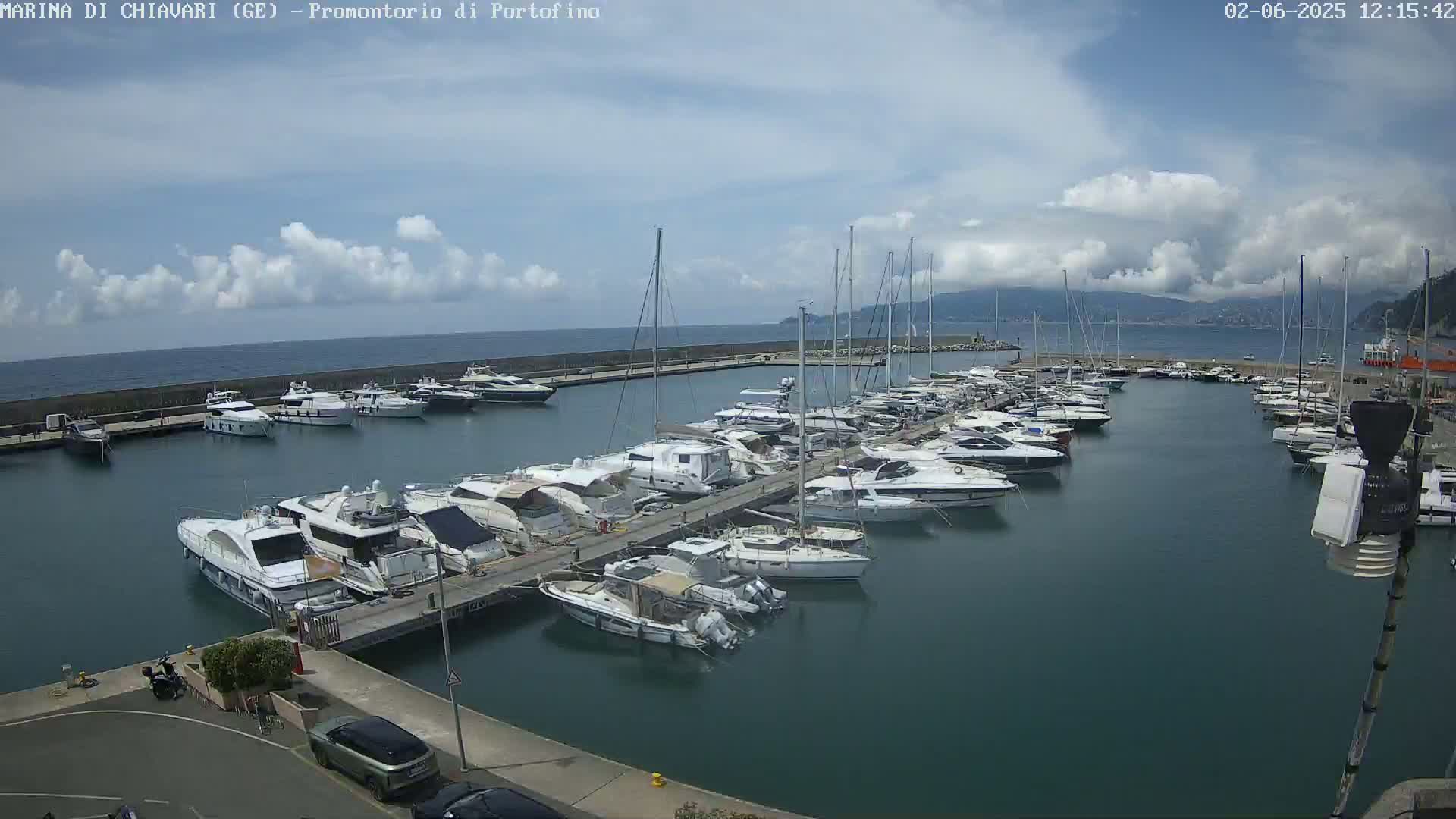 A marina filled with numerous yachts and sailboats is situated on a calm body of water under a partly cloudy sky.