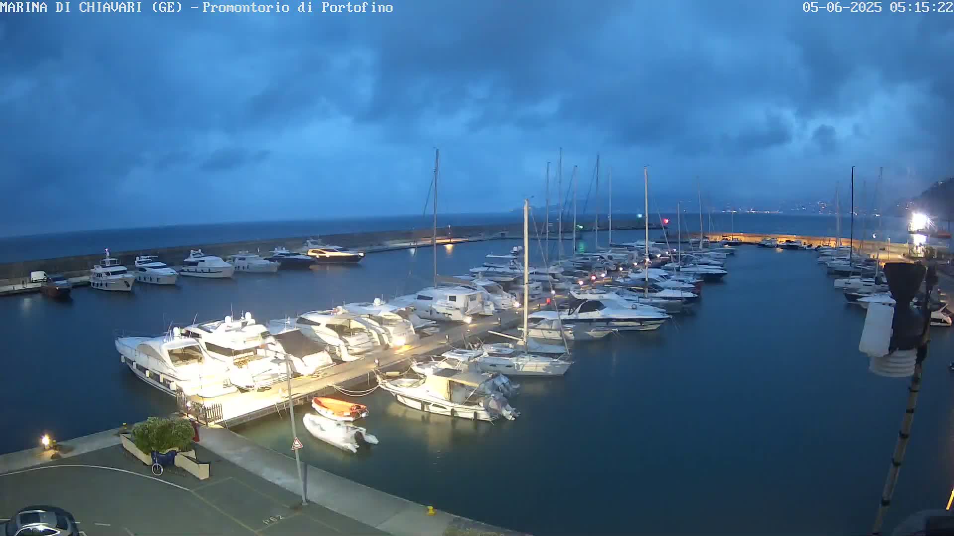 Many yachts and boats are docked in a marina at twilight under a cloudy sky.