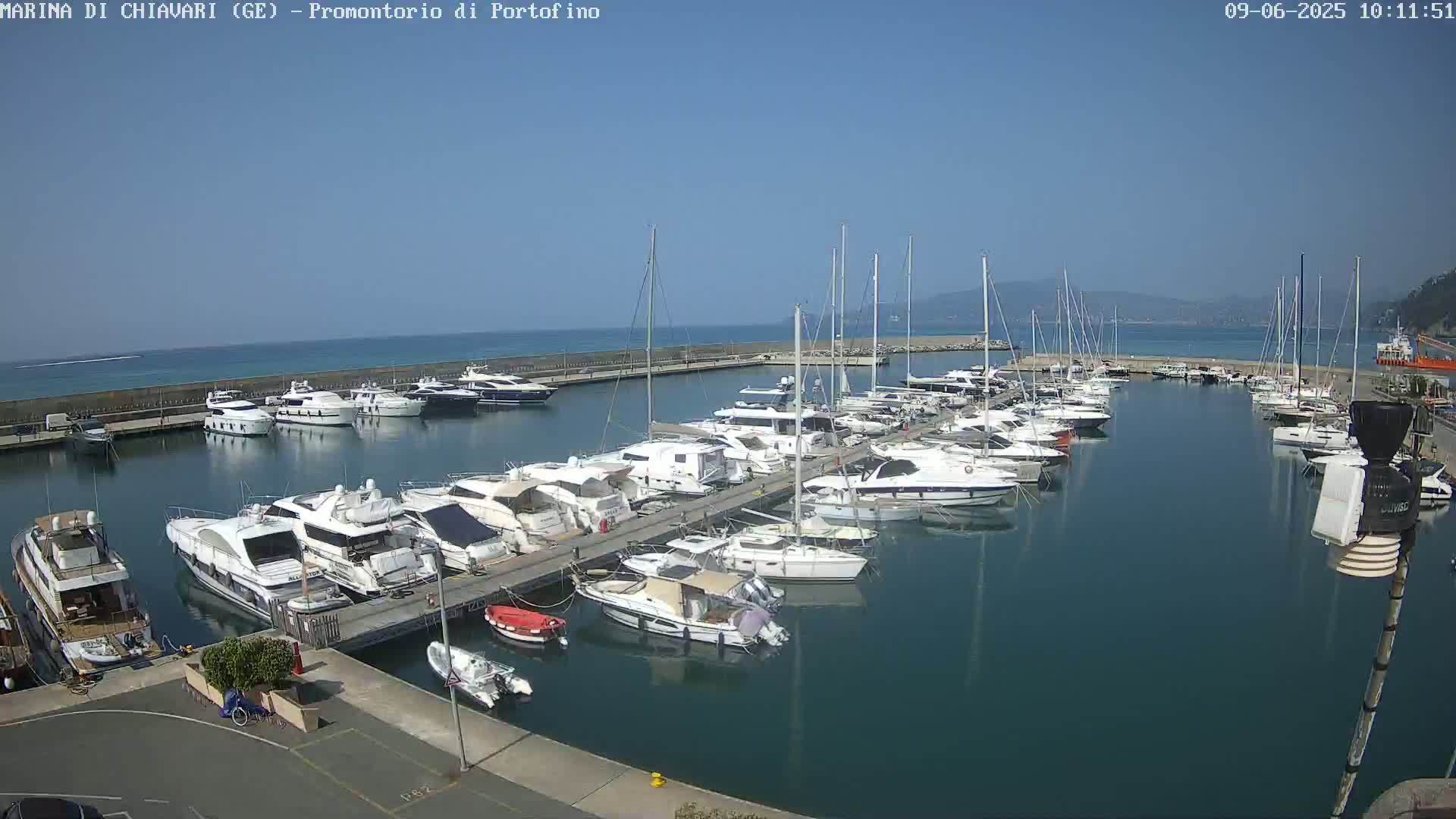 A marina filled with numerous yachts and sailboats on a sunny day, with calm, clear blue water.