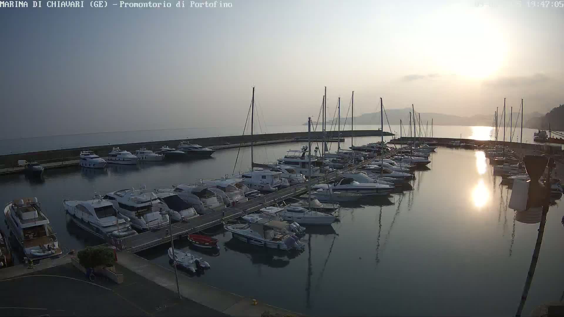 A marina filled with numerous boats and yachts is seen at sunset under a hazy sky.