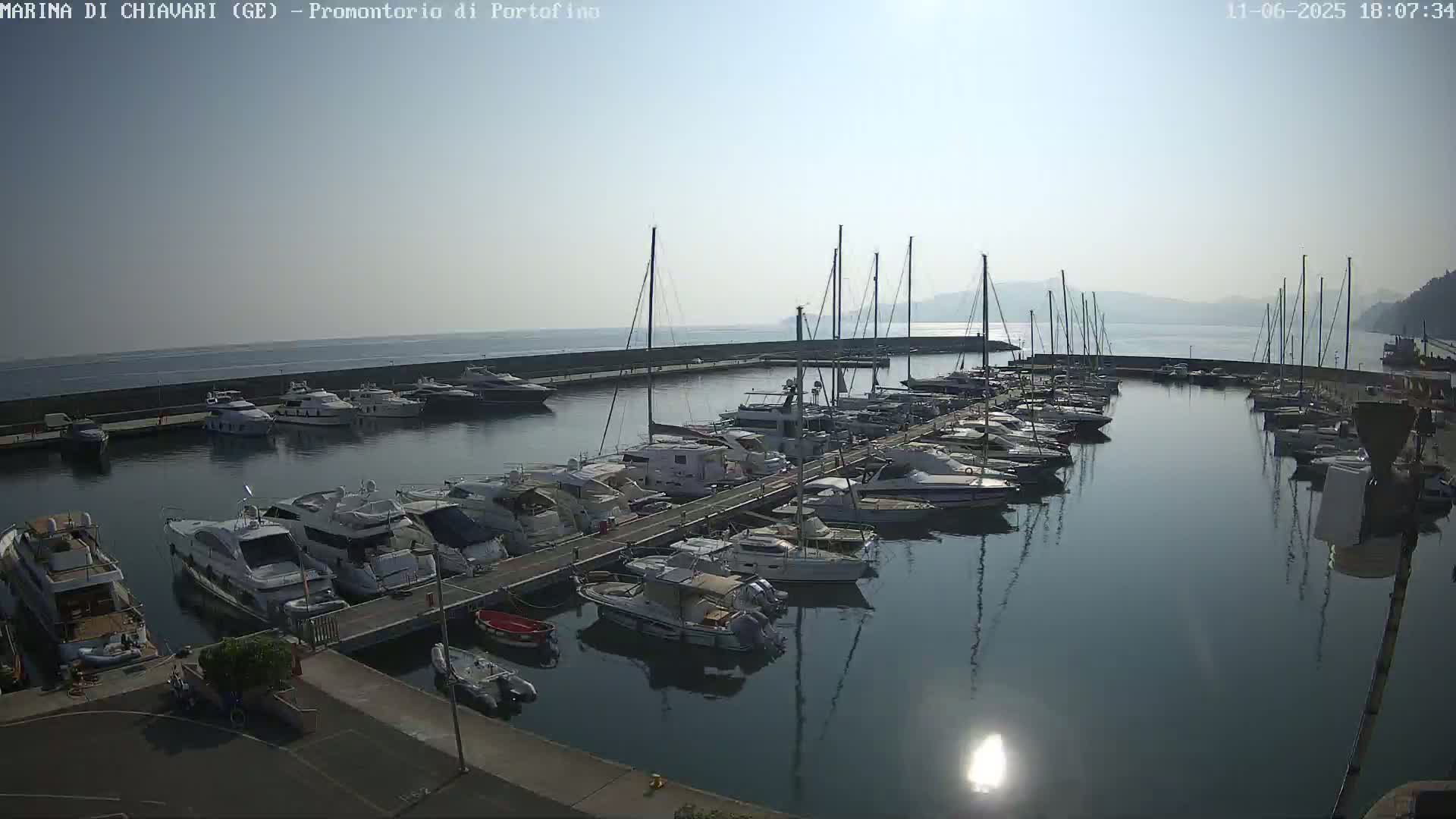 A marina filled with numerous boats and yachts is seen on a sunny day with calm waters.