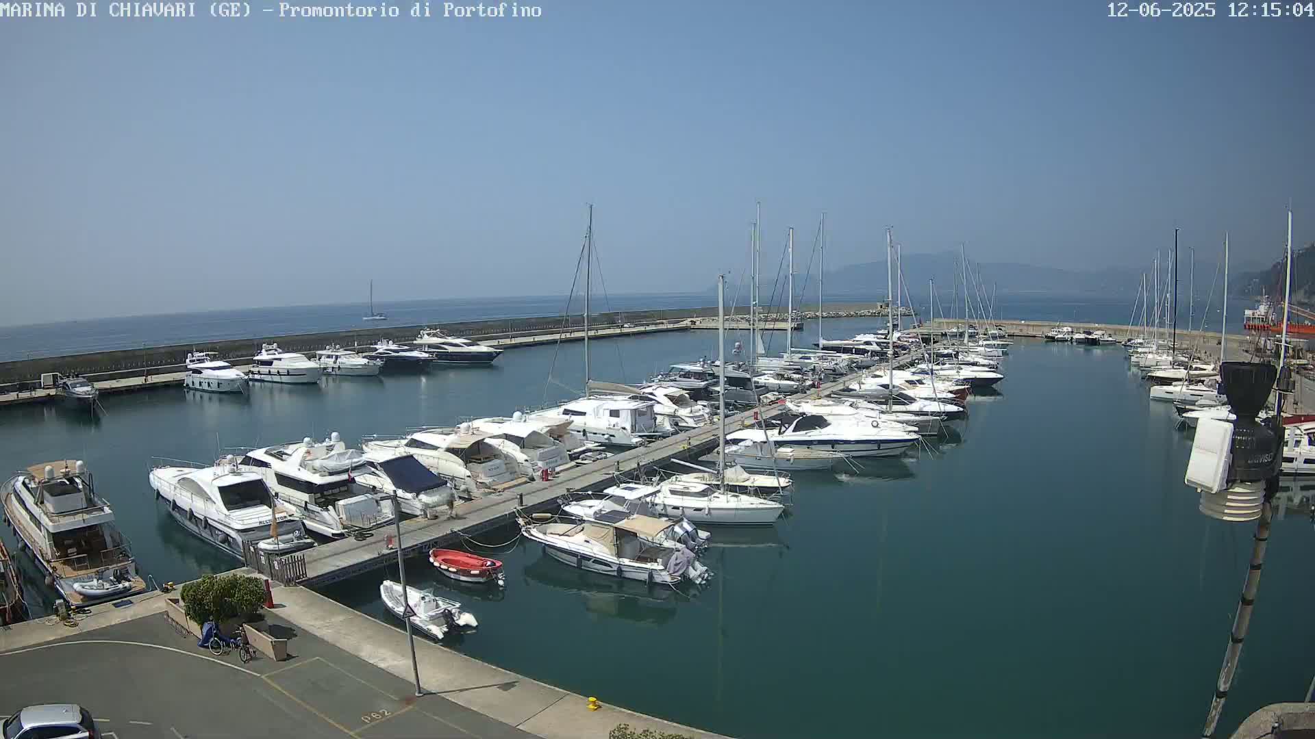 A marina filled with numerous yachts and sailboats is situated on calm, clear water under a bright sunny sky.