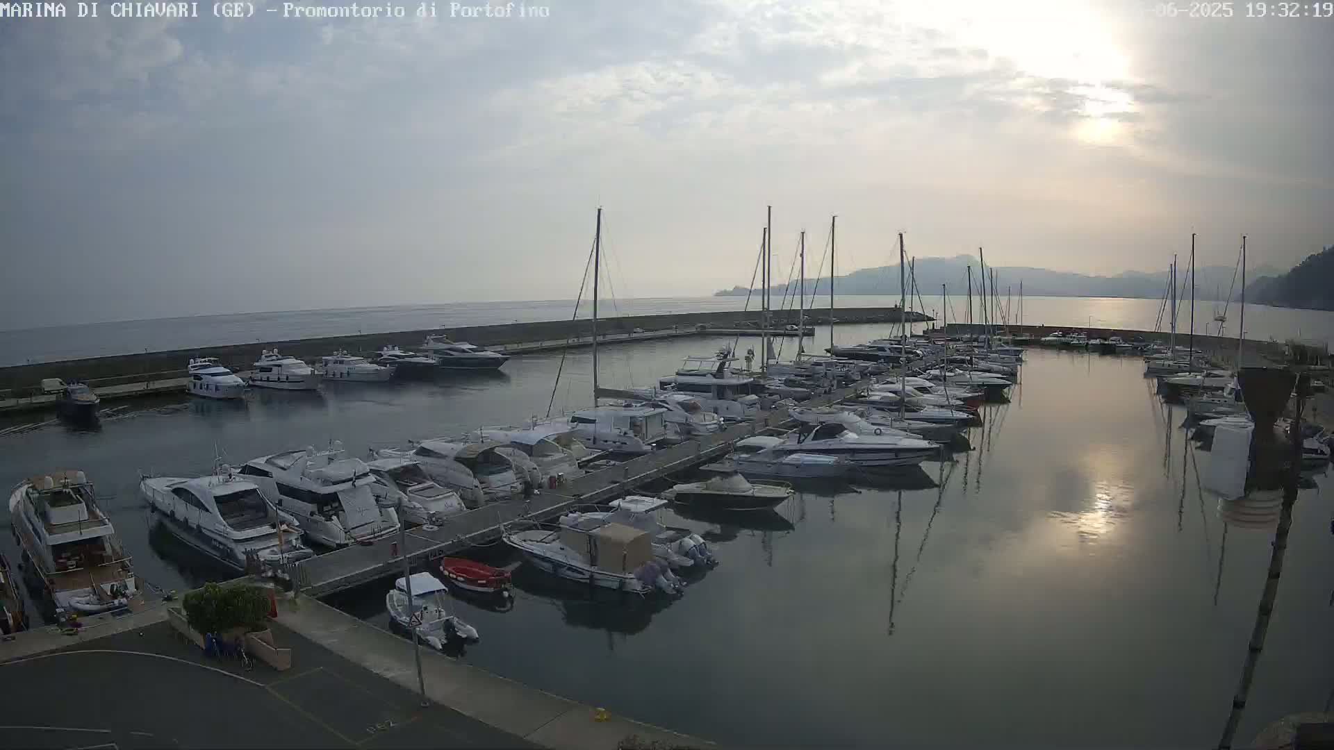 A marina filled with many yachts and sailboats is shown under a partly cloudy sky.