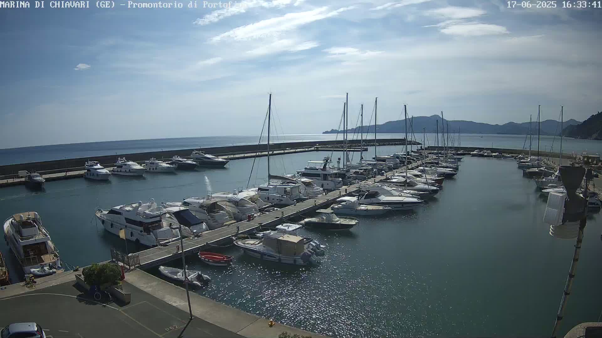 A marina filled with numerous yachts and sailboats is situated on calm water under a partly cloudy sky.
