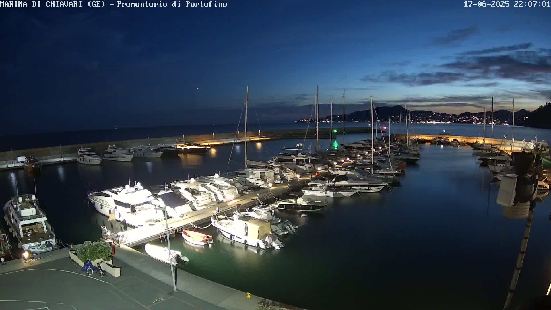 Many yachts and boats are docked in a marina at twilight under a mostly clear, dark blue sky.