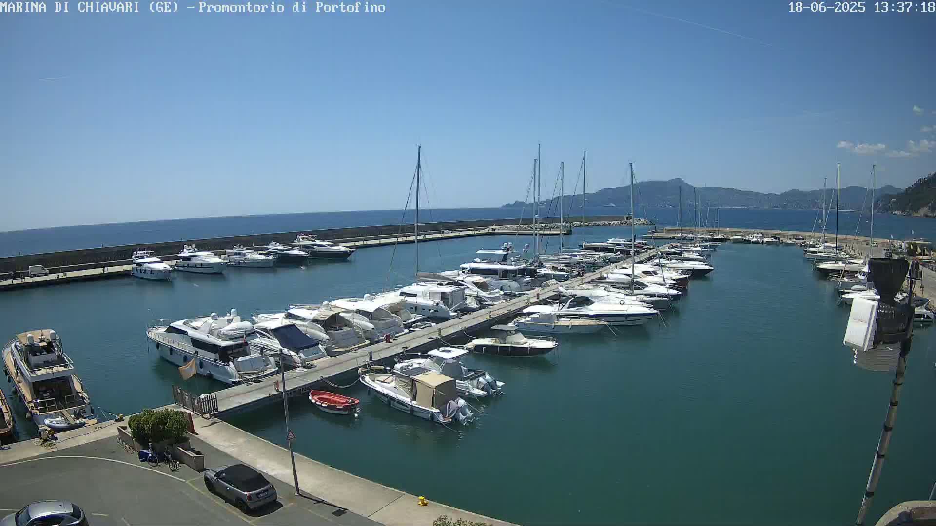 A marina filled with numerous yachts and boats is shown on a sunny day with clear blue skies and calm water.