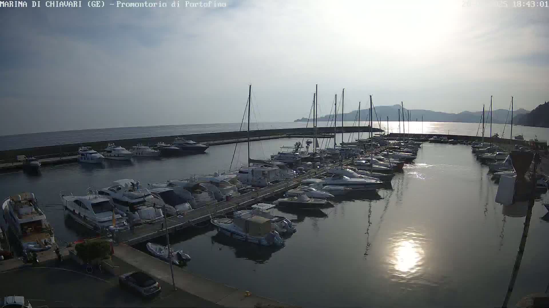 A marina filled with numerous boats and yachts is shown under a partly sunny sky.